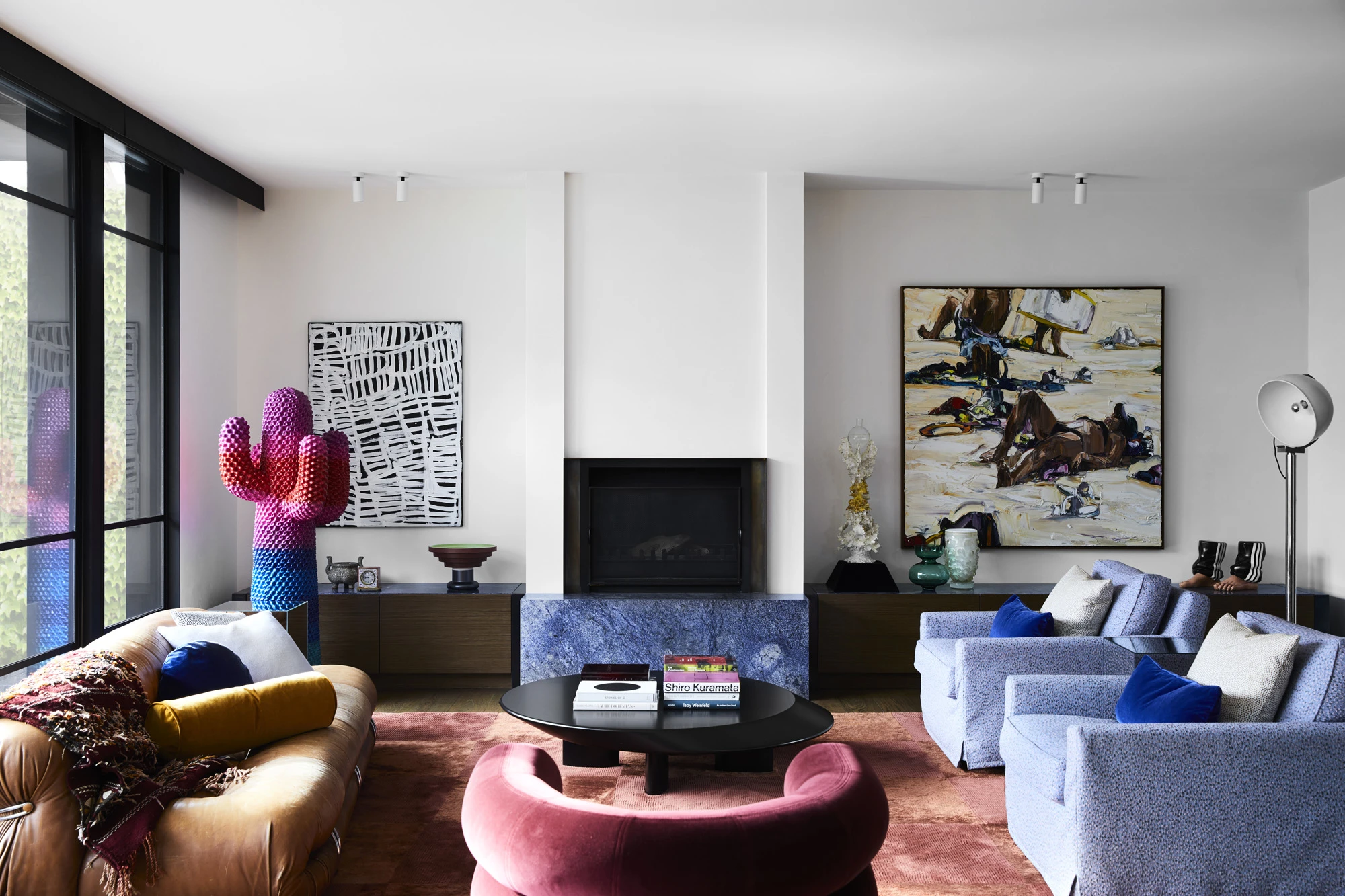 White living room with pink velvet armchair, blue armchairs, brown couch, large artworks