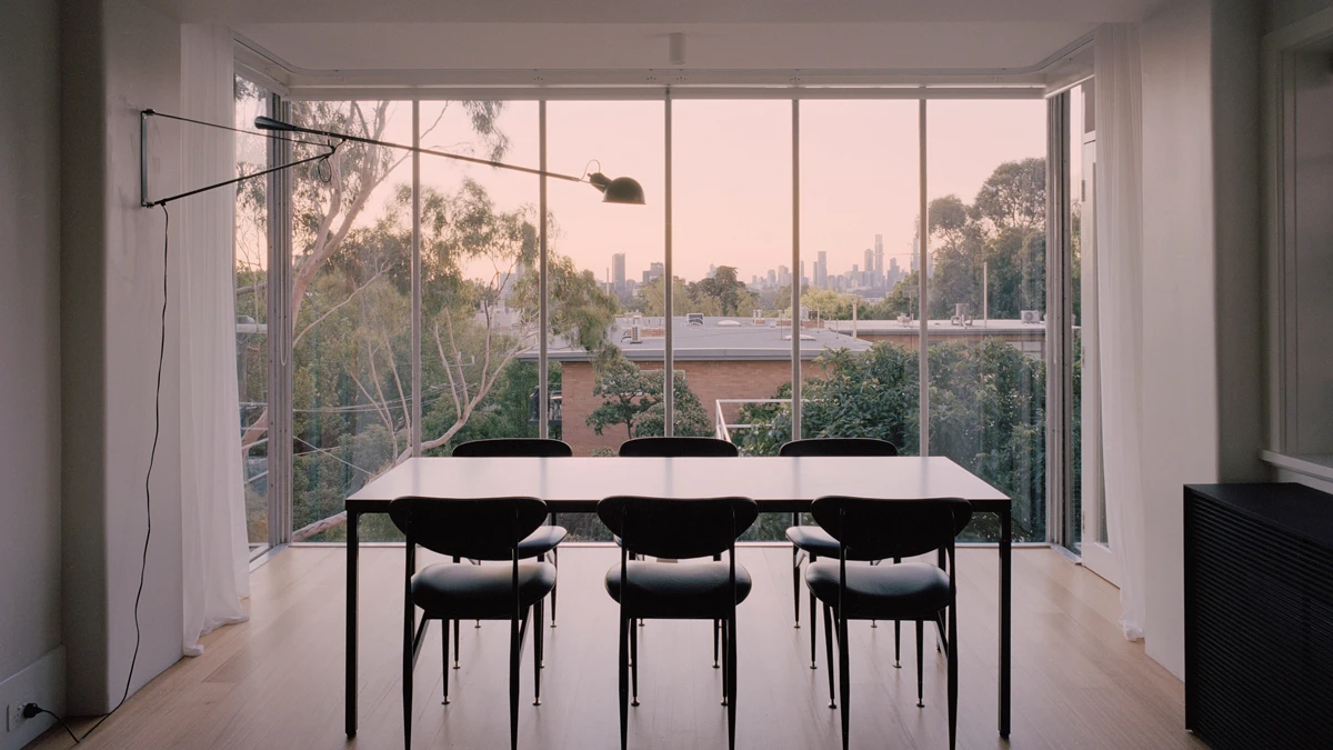 Dining table and chairs looking out large floor to ceiling windows. 