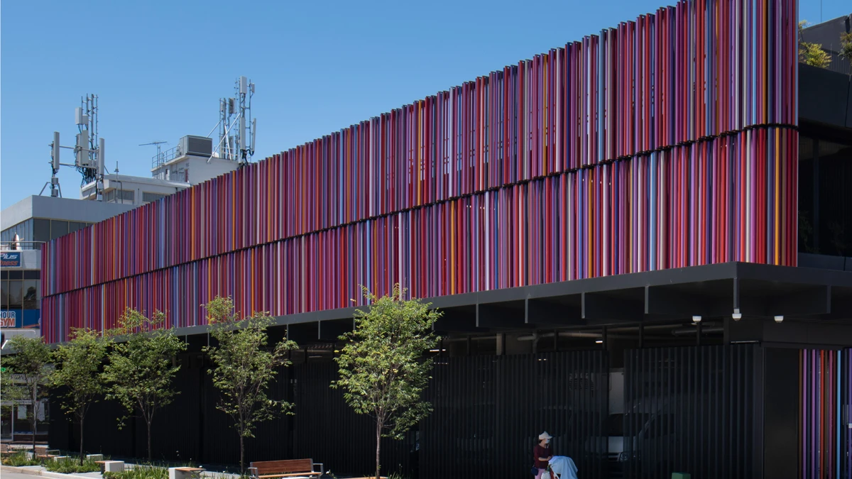 Exterior of carpark with trees on outside. Panels of carpark in various pink, purple, and red shades.