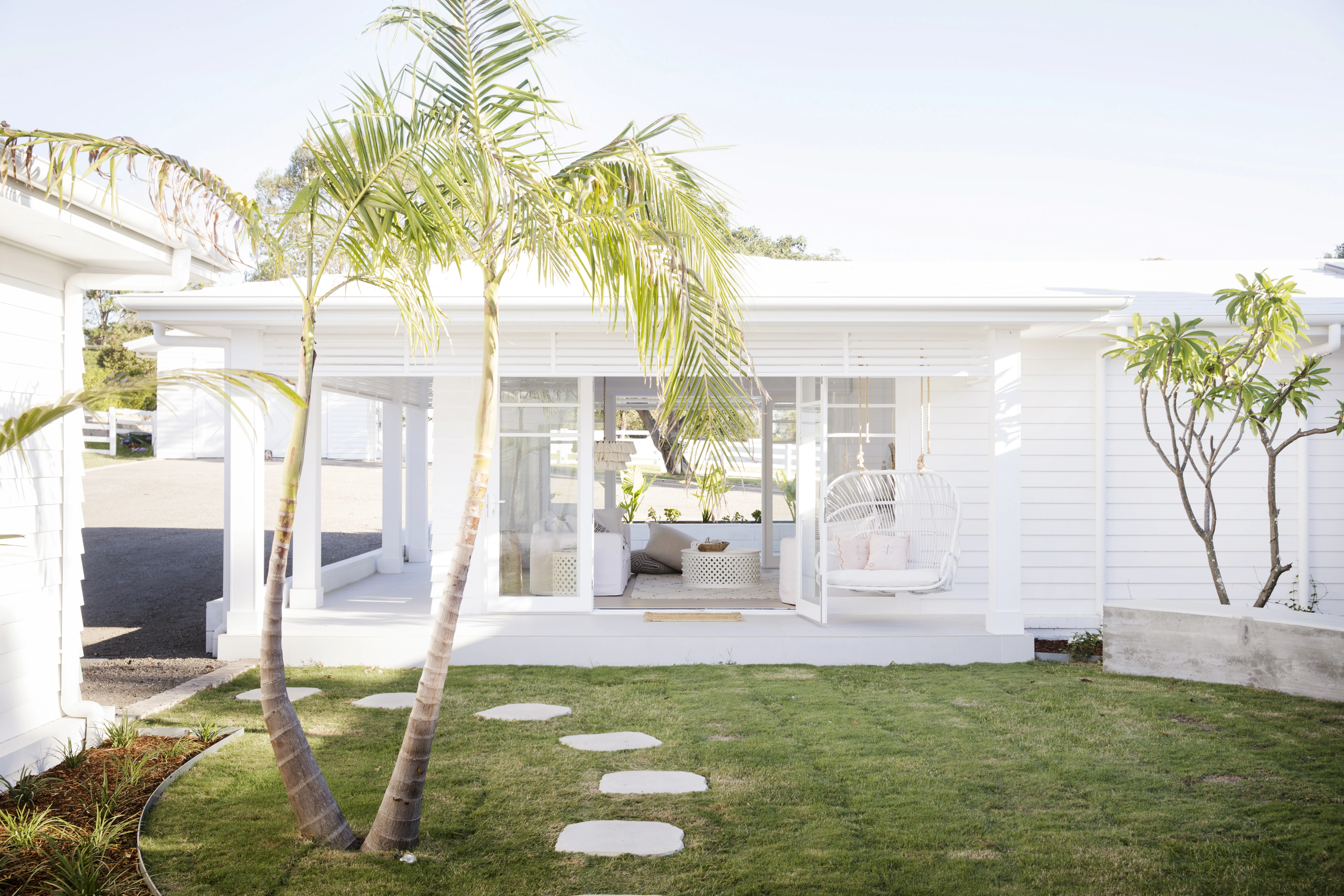 Low ceiling 70's style home with palm trees in front garden painted in white. 