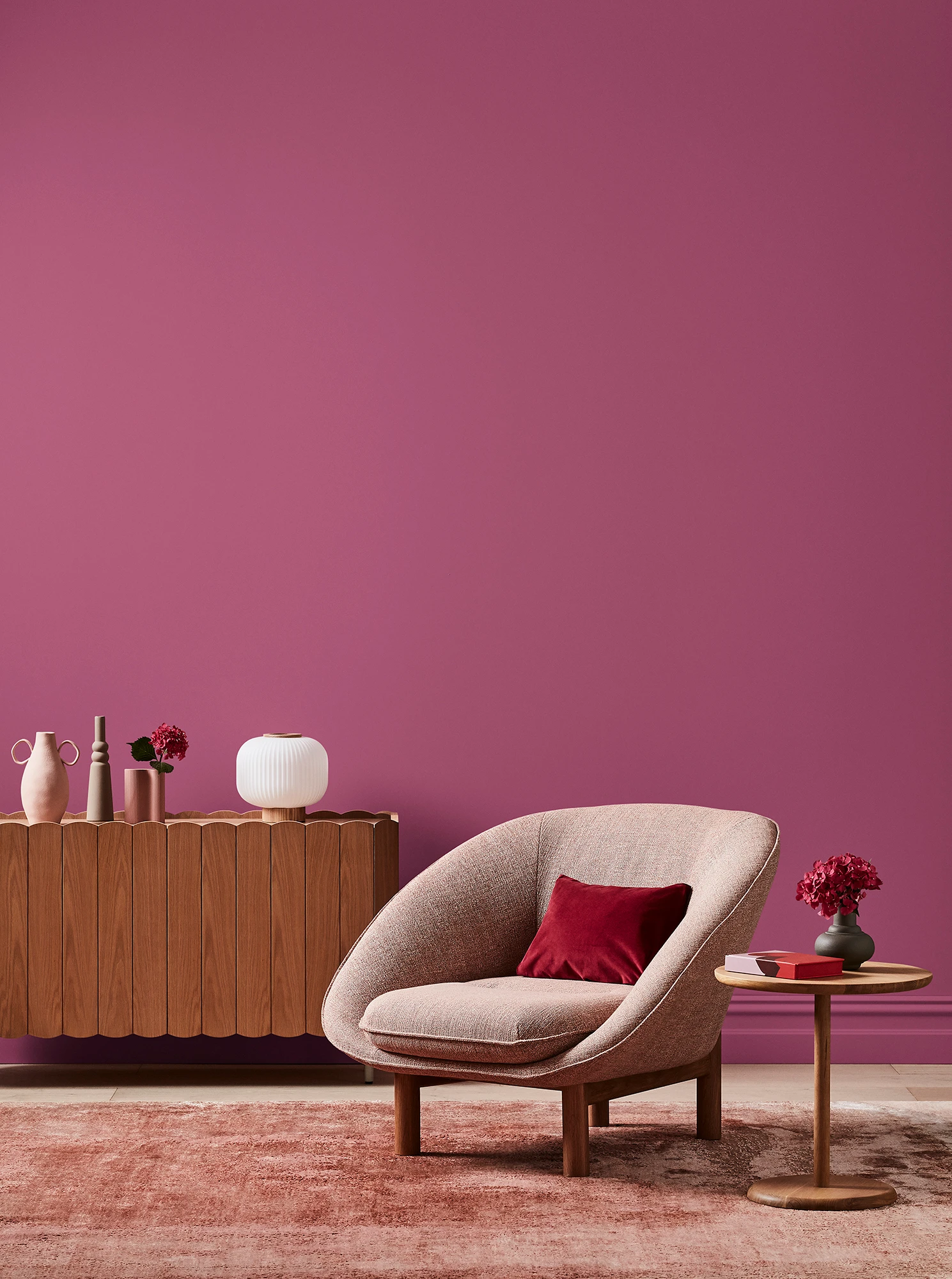 Deep pink living room with pink armchair, wooden side table and sideboard with white and pink decor.