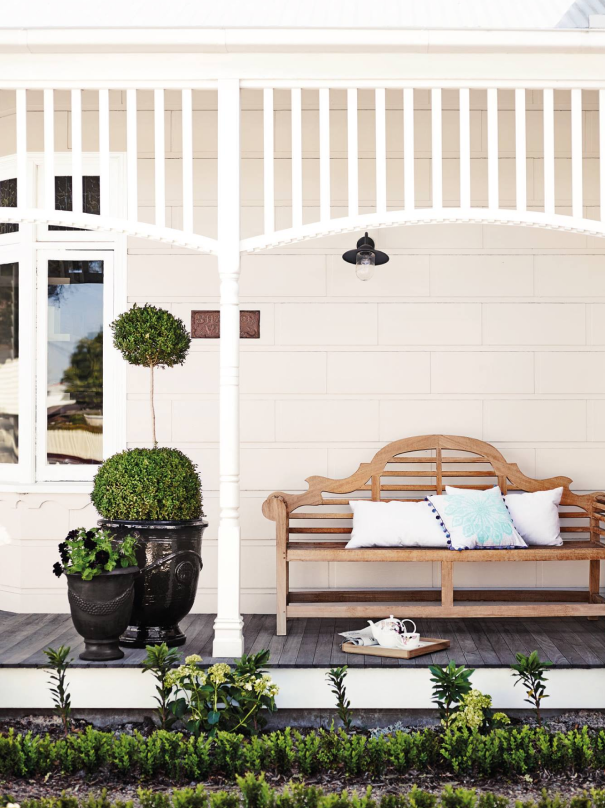 White verandah of traditional home with wooden bench and topiary English box plants.