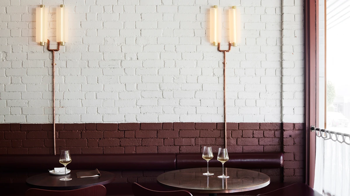 Tables with wine glasses against painted brick wall with light attachments.