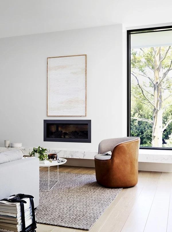 Modern living room with white ceiling and walls. Large plate window, inset fireplace and brown leather chair