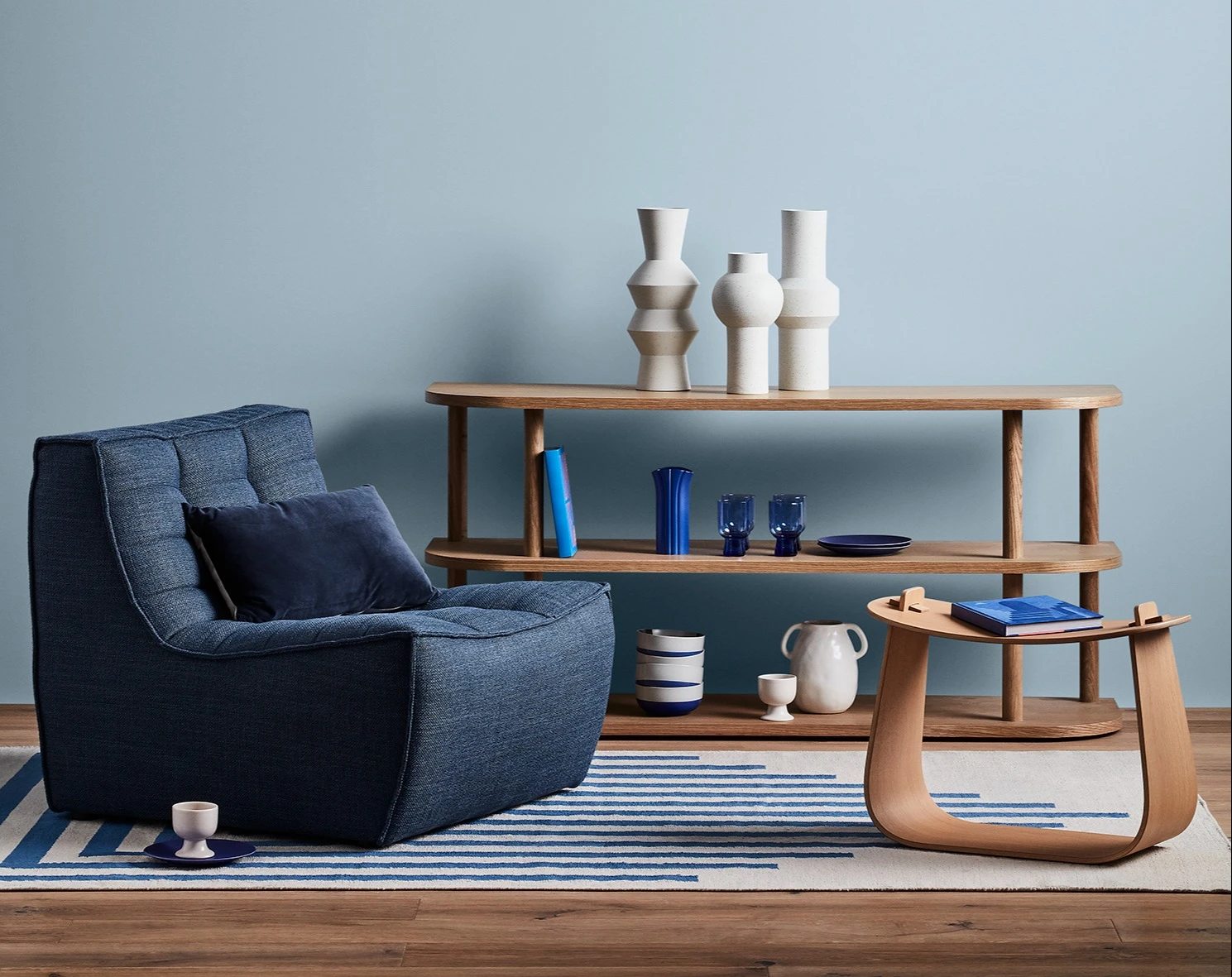 Blue themed lounge room with cushioned chair and decorative items on a hallway table. 