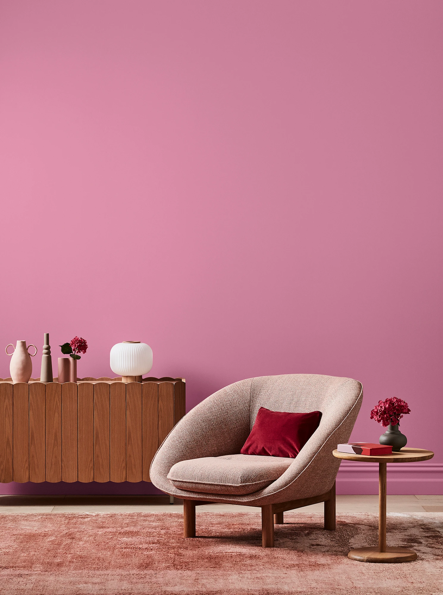 Deep pink living room with pink armchair, wooden side table and sideboard with white and pink decor.