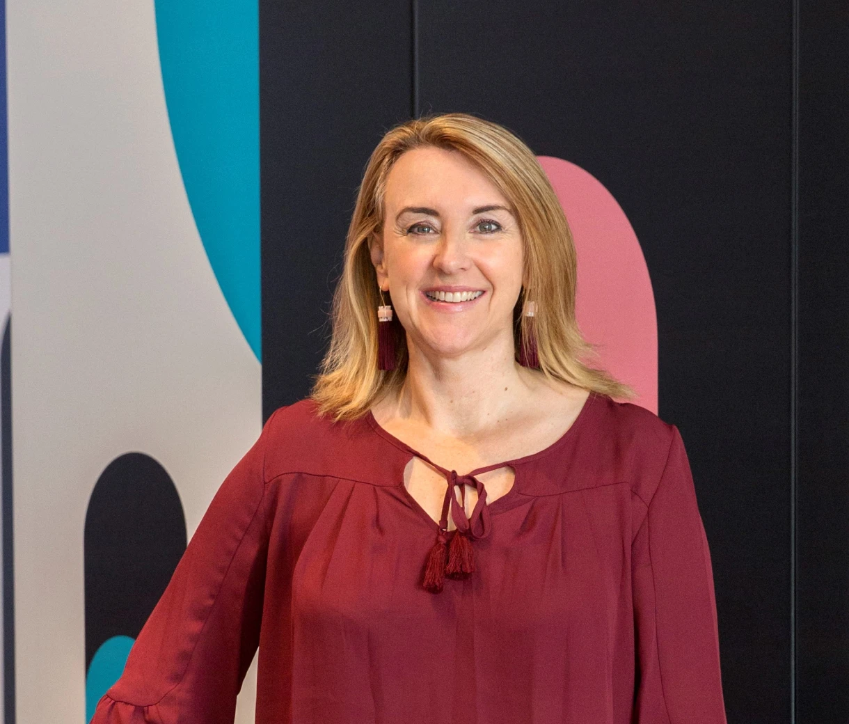 Portrait photo of Colour team member Andrea in front of a black and white wall with pops of blue and pink colour.