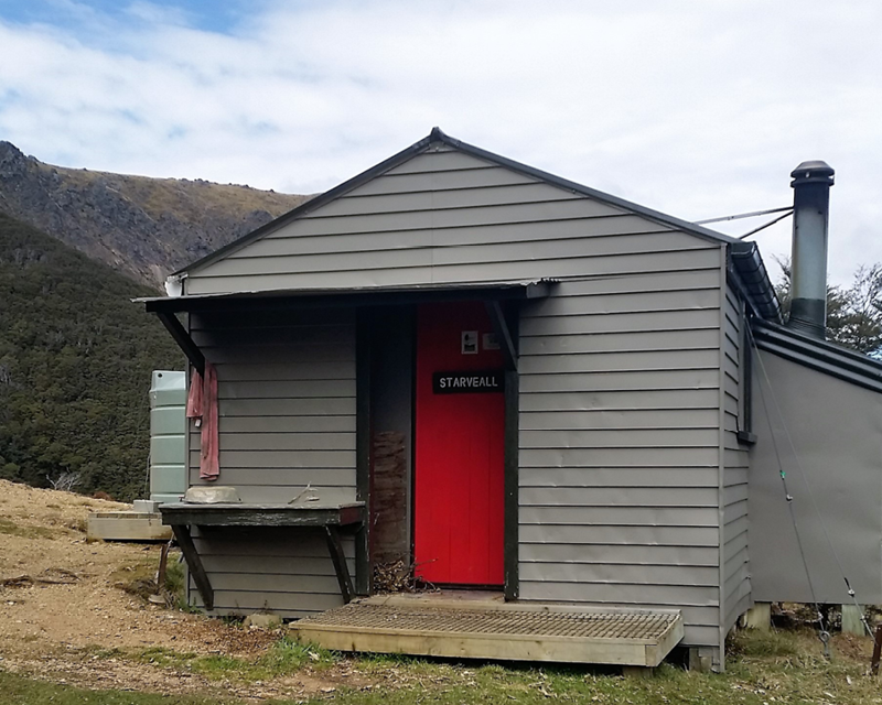 Starveall Hut has a red door and grey exterior
