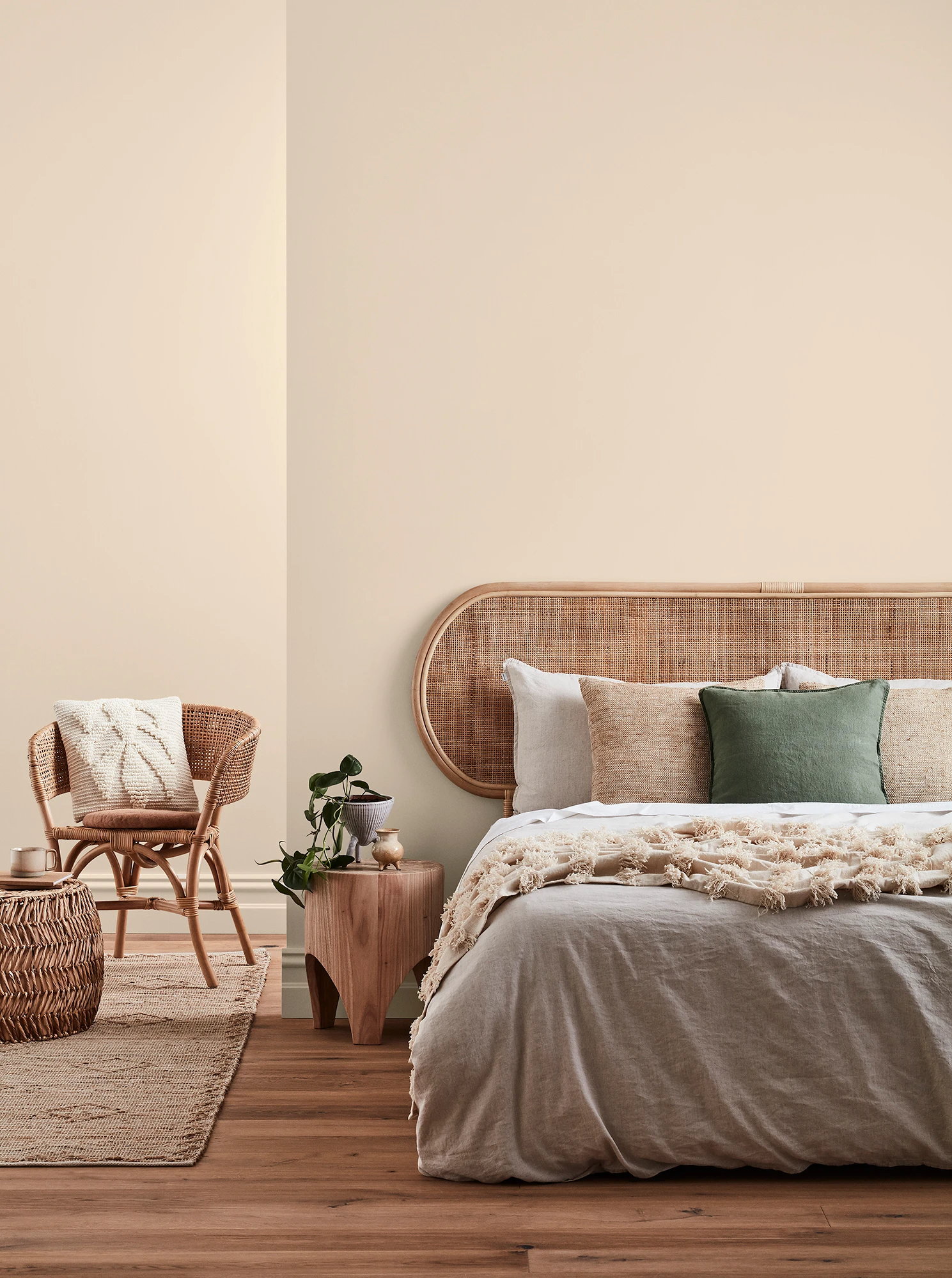 Neutral-coloured bedroom with rattan headboard and chair and neutral linens.