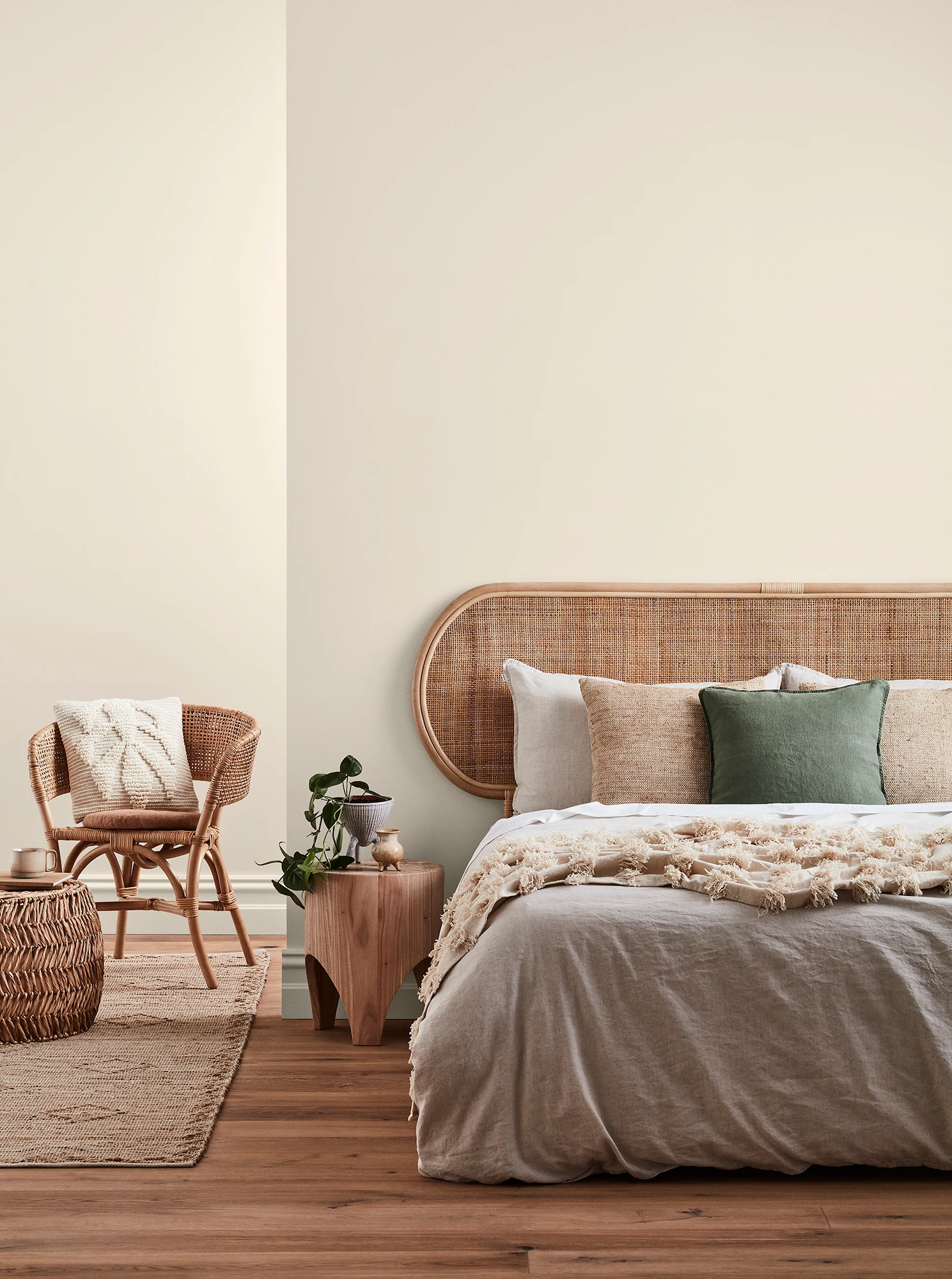 Neutral-coloured bedroom with rattan headboard and chair and neutral linens.