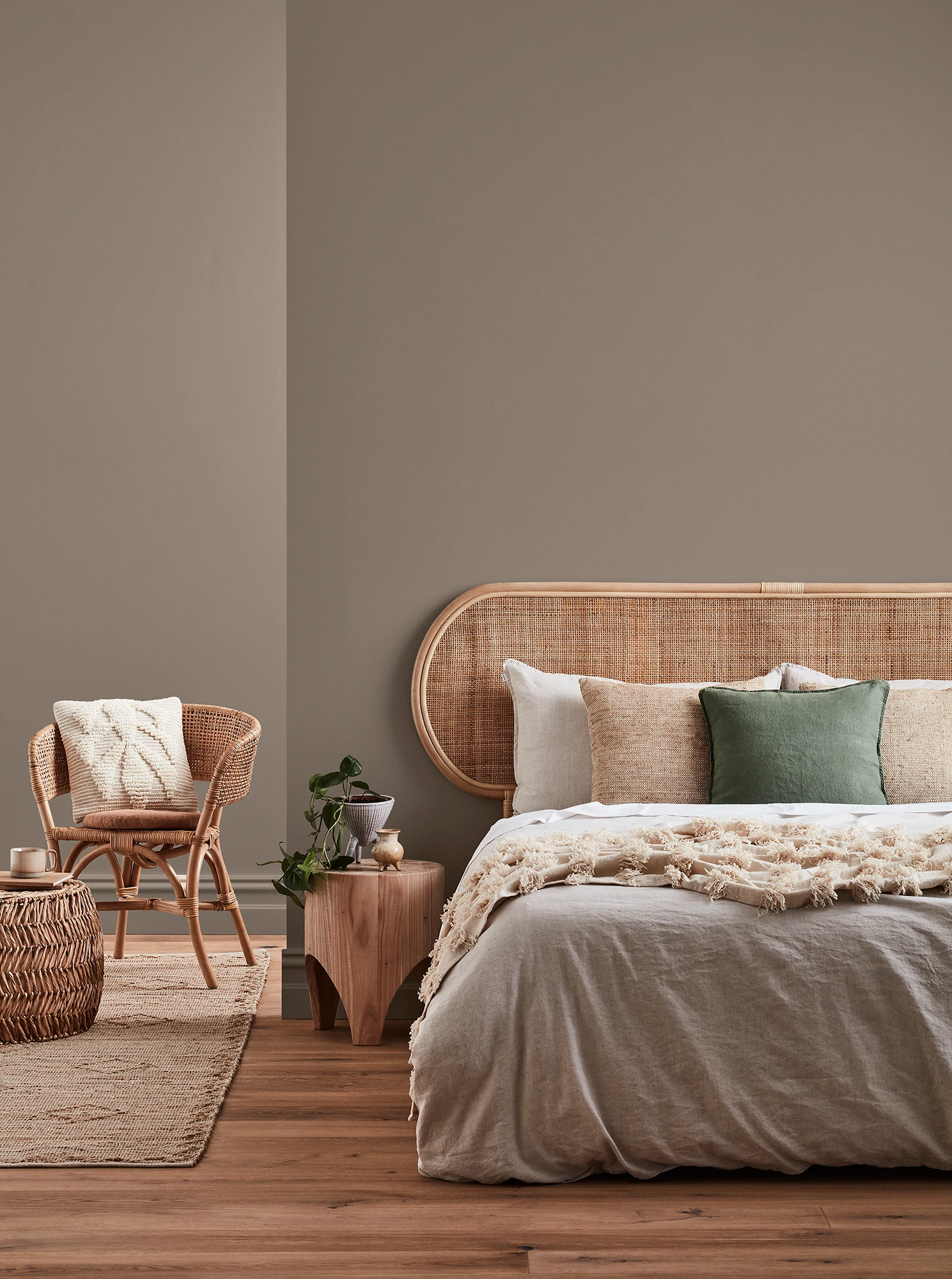 Neutral-coloured bedroom with rattan headboard and chair and neutral linens.