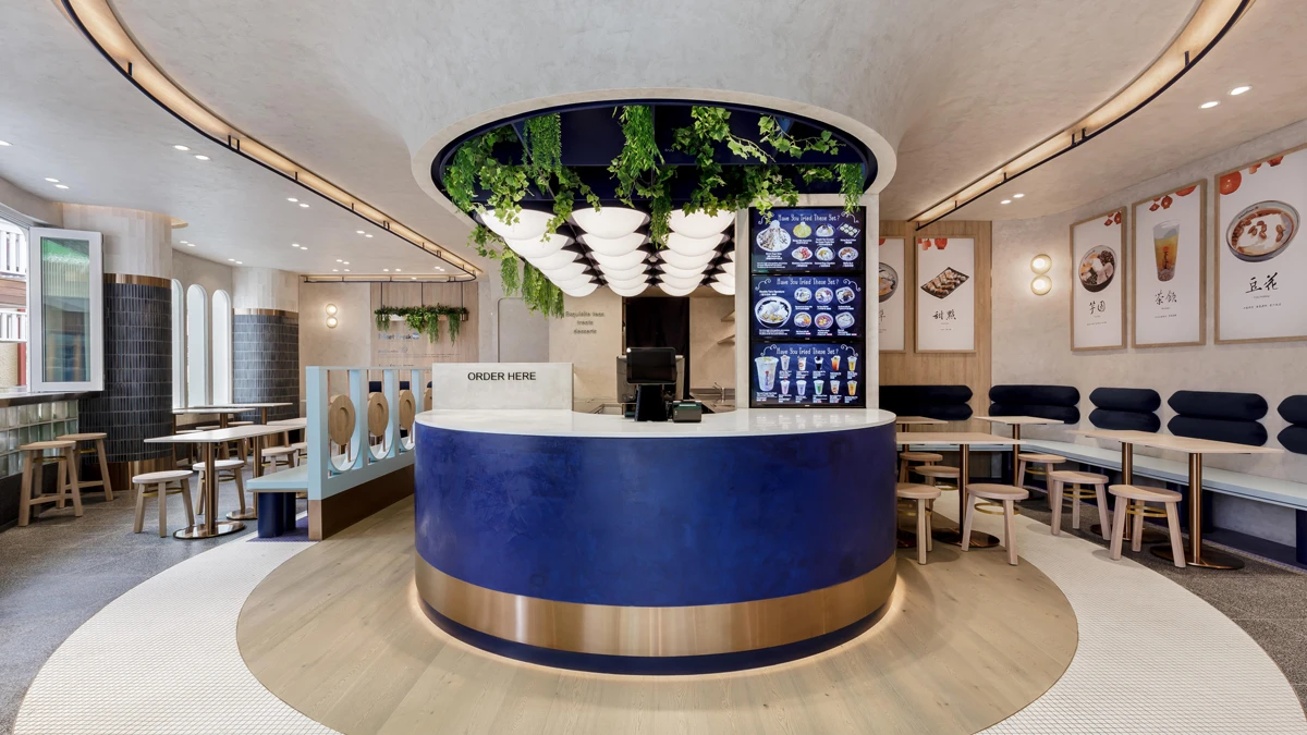 Blue circular bar in middle of room with greenery above bar and seating to sides and wall. 