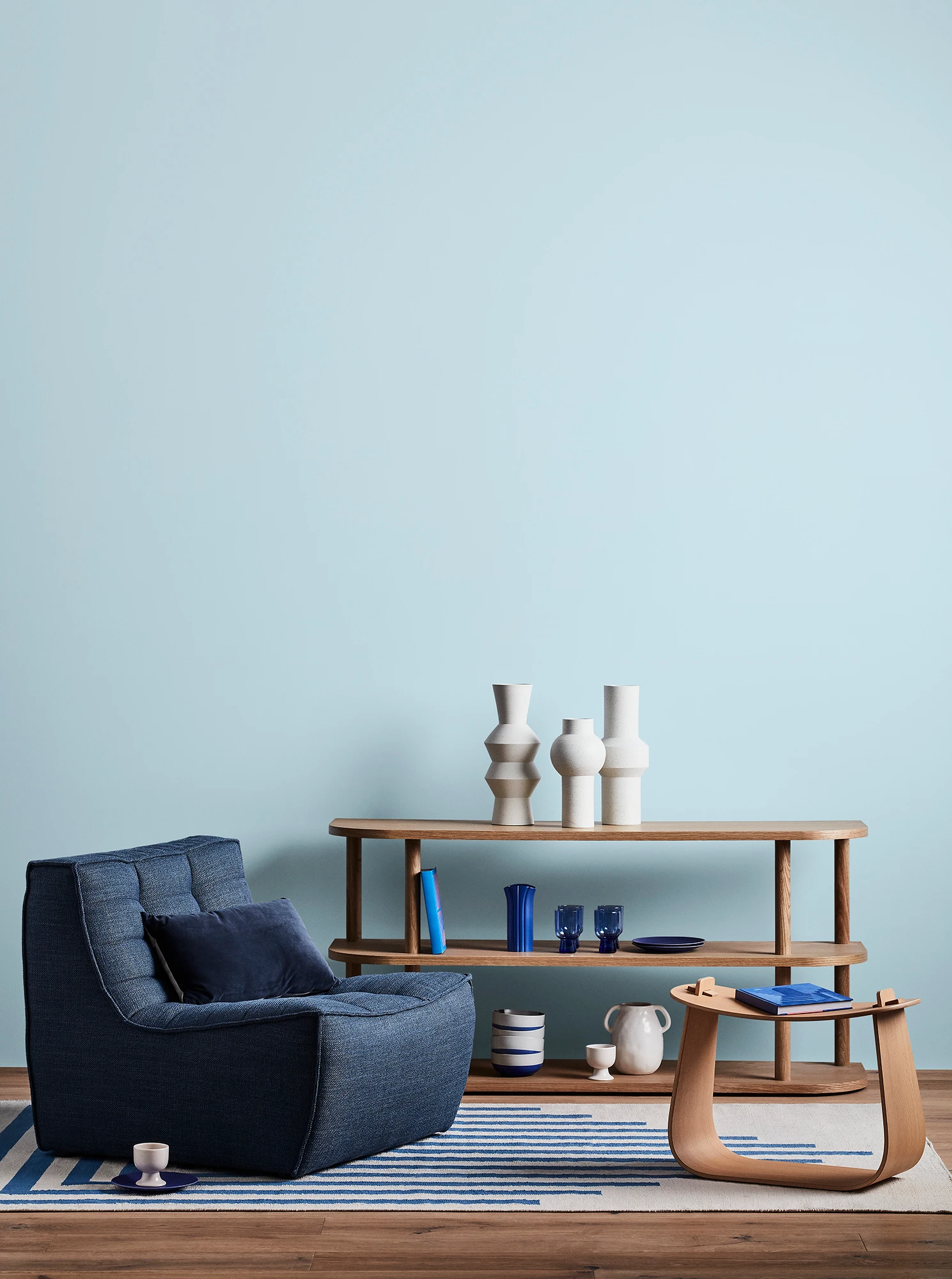 Blue living room with blue armchair, wooden coffee table and shelves with blue and white decor.  