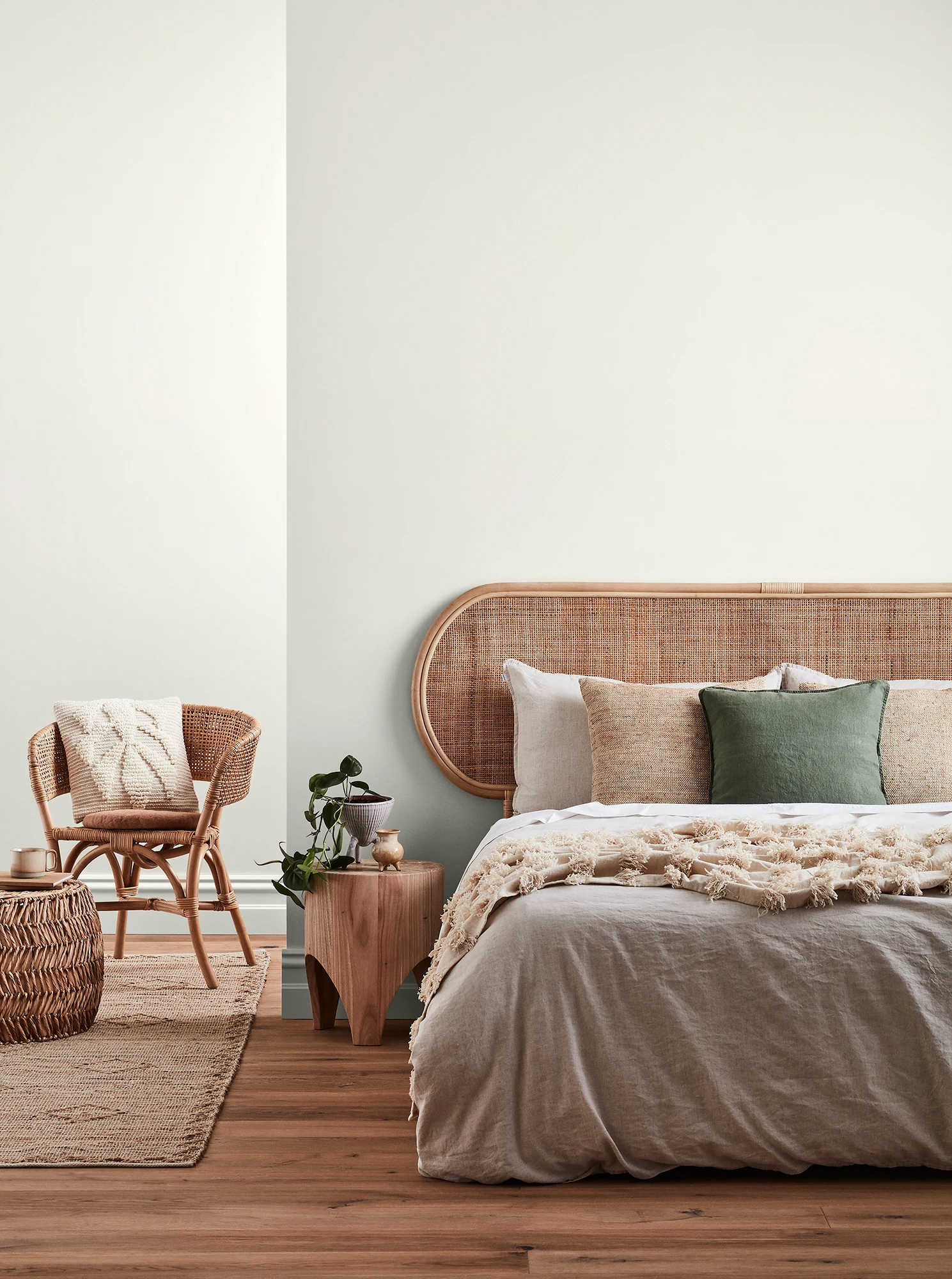 Neutral-coloured bedroom with rattan headboard and chair and neutral linens.