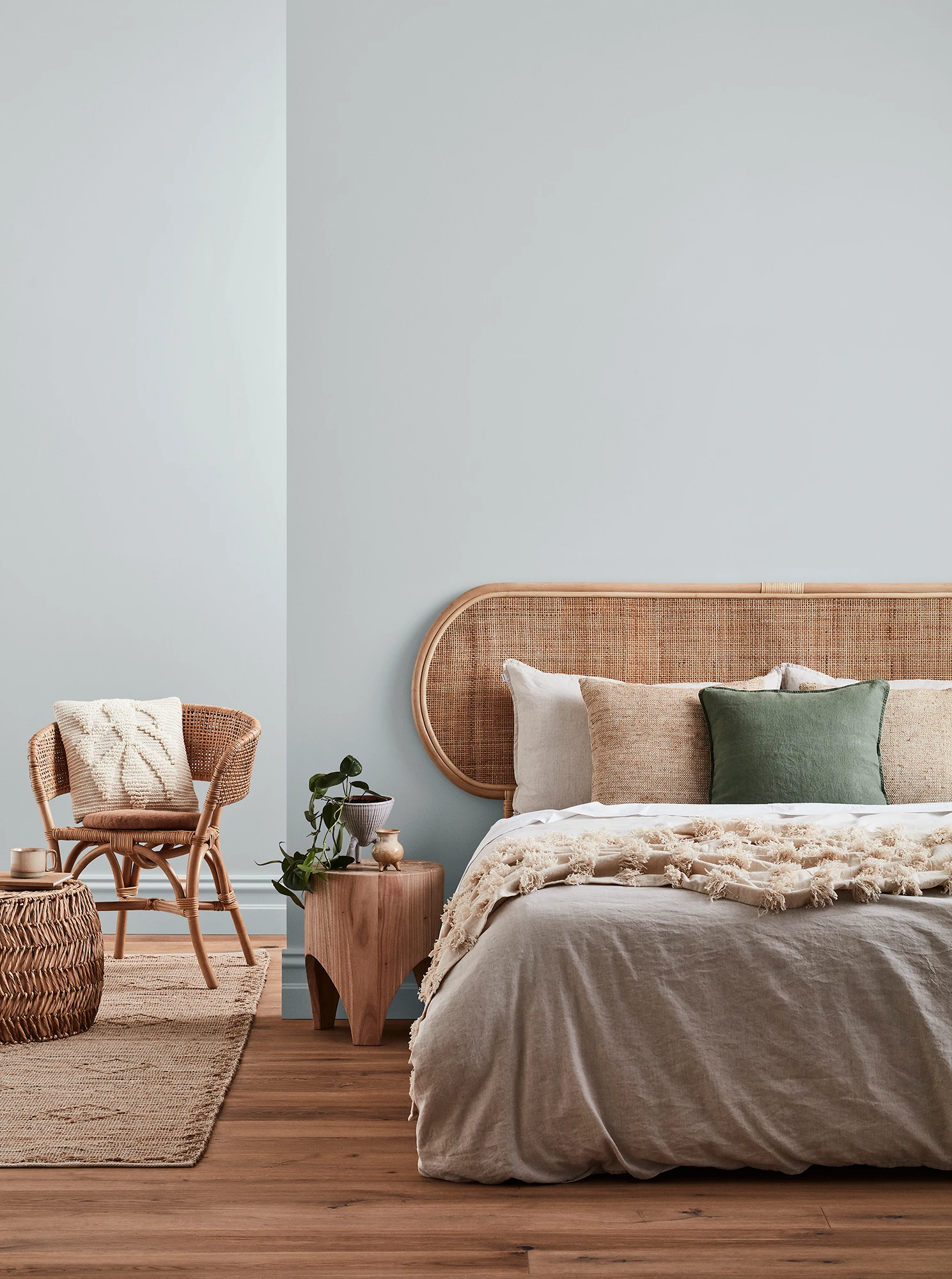 Neutral-coloured bedroom with rattan headboard and chair and neutral linens.