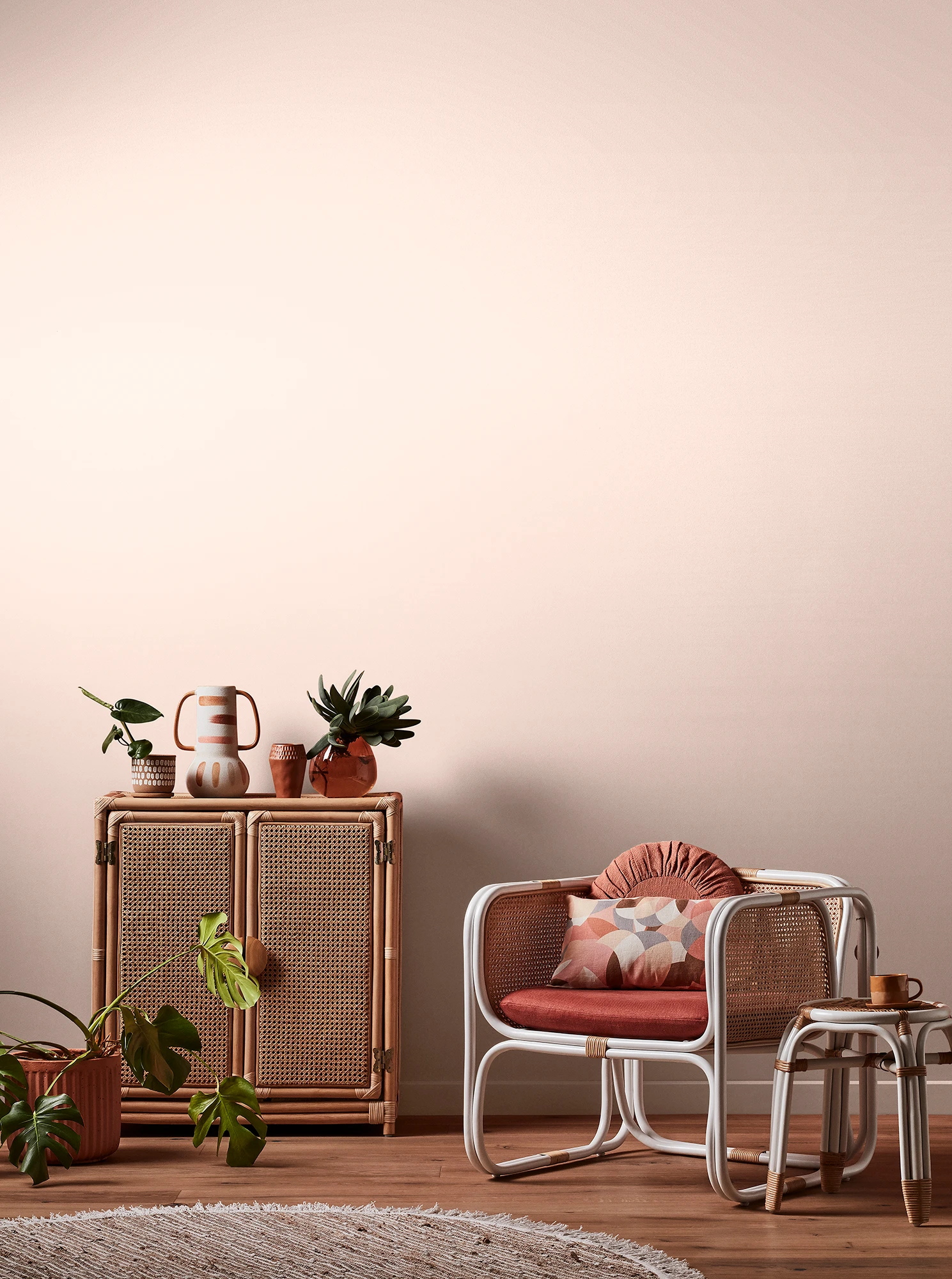 Light orange-neutral living room with natural rattan cabinet and white rattan table and chair with pink cushions.