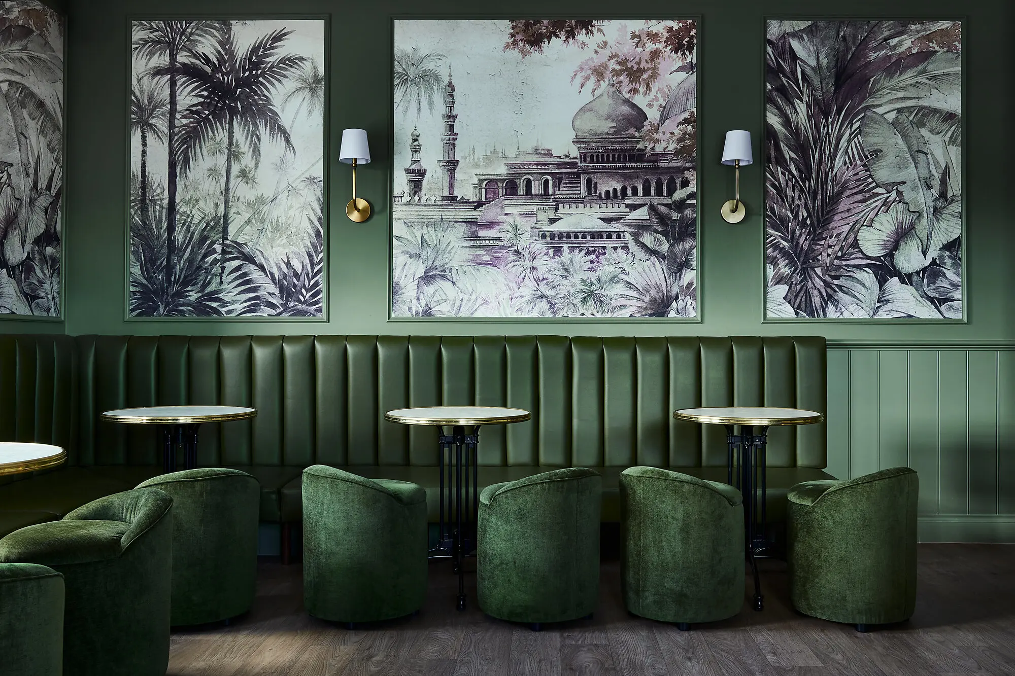 Green-themed seating area with paintings on wall and small velvet circular chairs. 