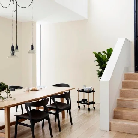 Interior wooden dining table with black chairs and hanging lights above. Staircase to side.