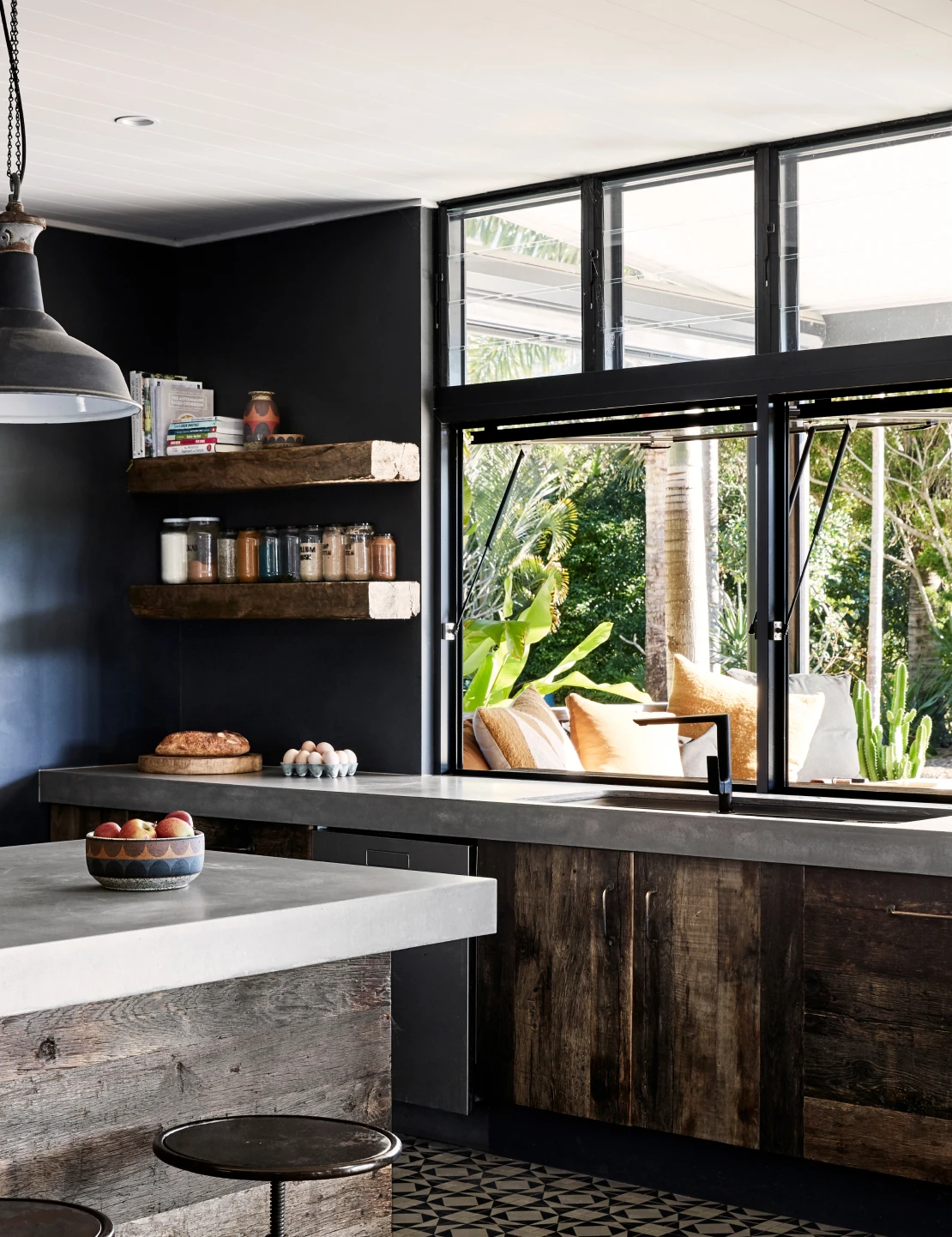 Kitchen window with Domino coloured walls, aged wood cabinets and shelves and concrete look bench tops.