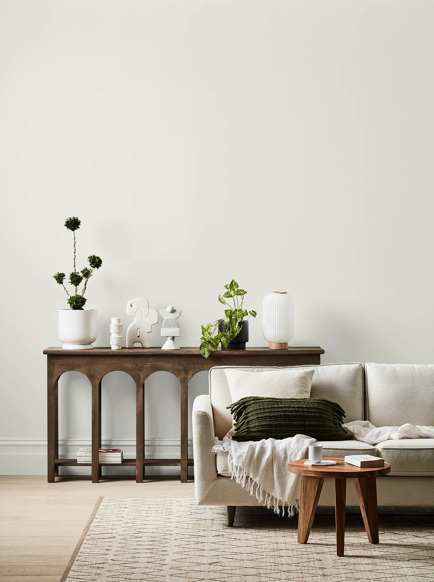 White living room with cream couch, timber side table and timber table with ornaments and plants.