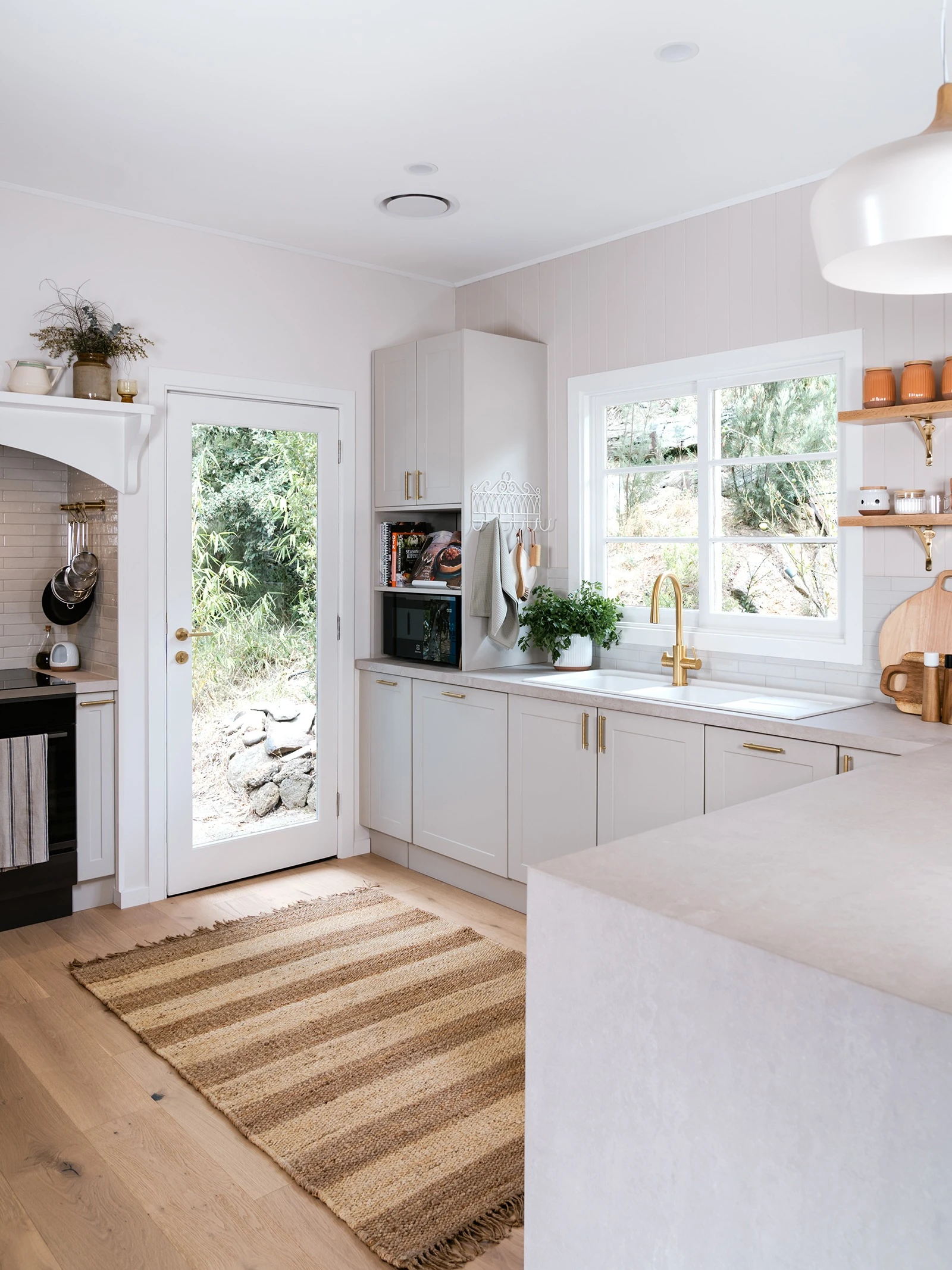 White neutral kitchen with stone benchtops and a jute rug on oak flooring