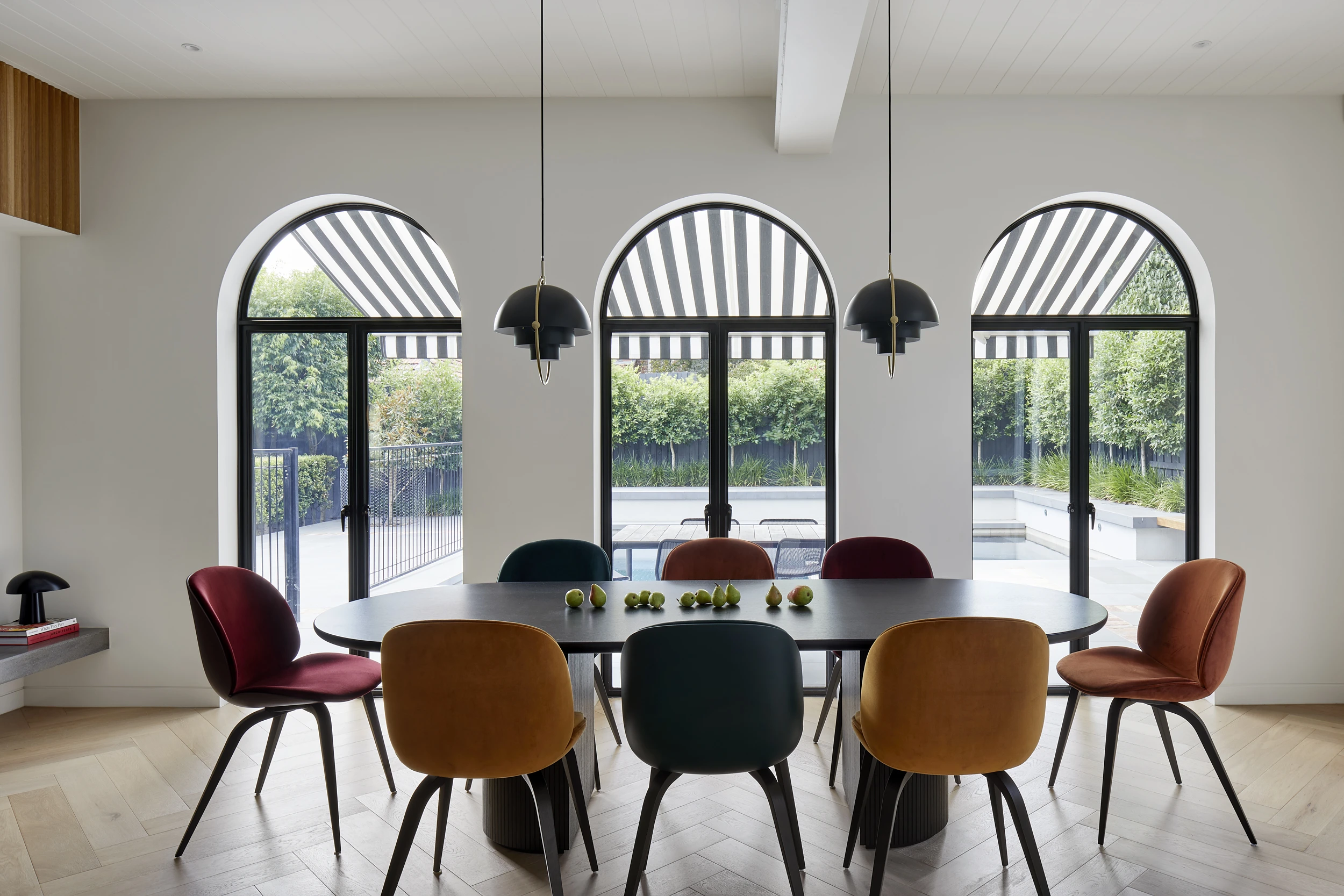 Arched windows behind dining table with low hanging lights. 