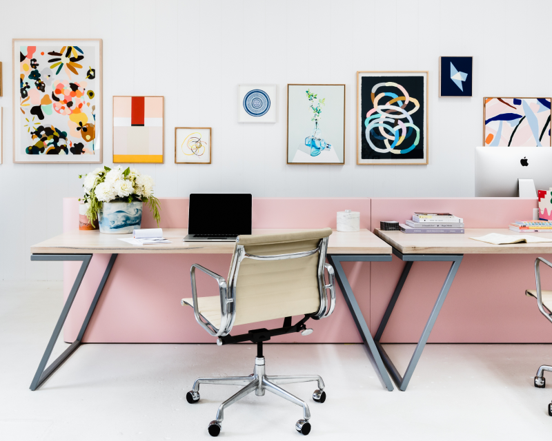 Pink and white office with art on walls.