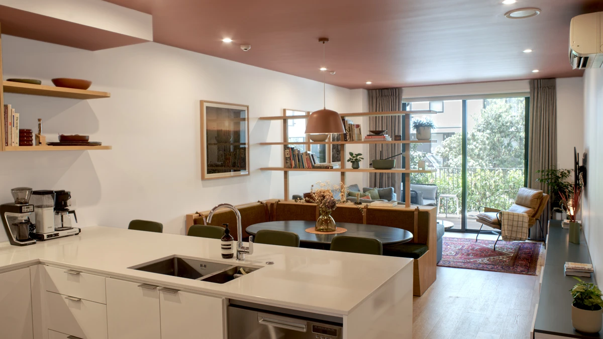 View from kitchen into living area separated by shelving with books. Various decorative items.