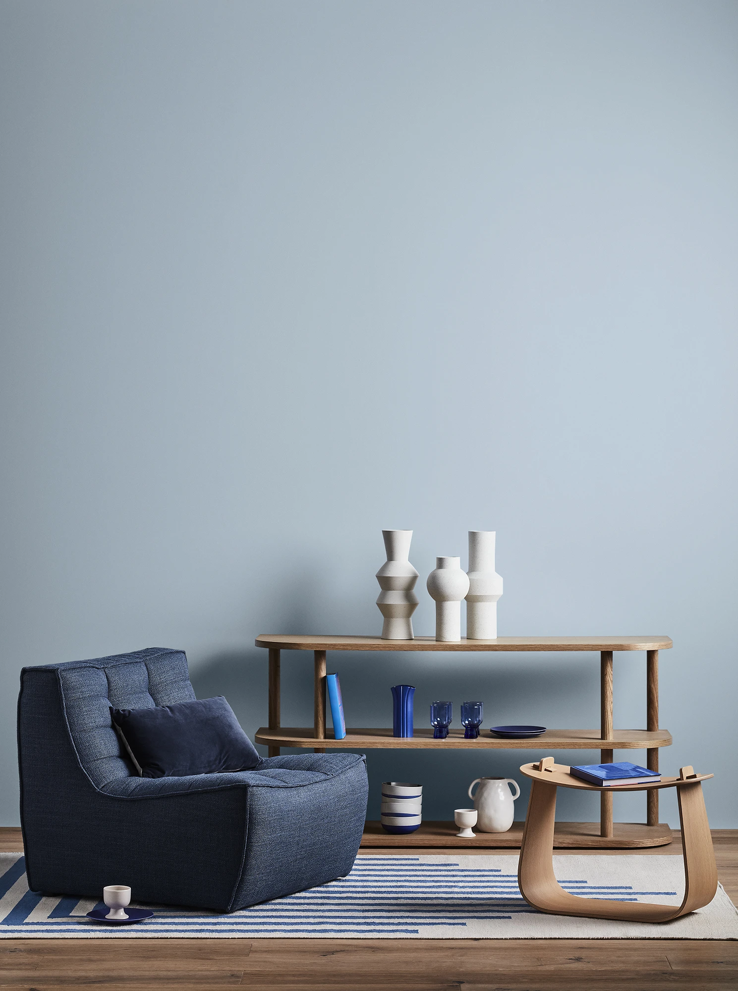 Blue themed lounge room with cushioned chair and decorative items on a hallway table. 