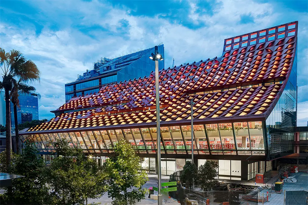 The exterior of the building showing the unique roof that is shaped, looking like spikes. The walls are glass and the building is sloped upwards.