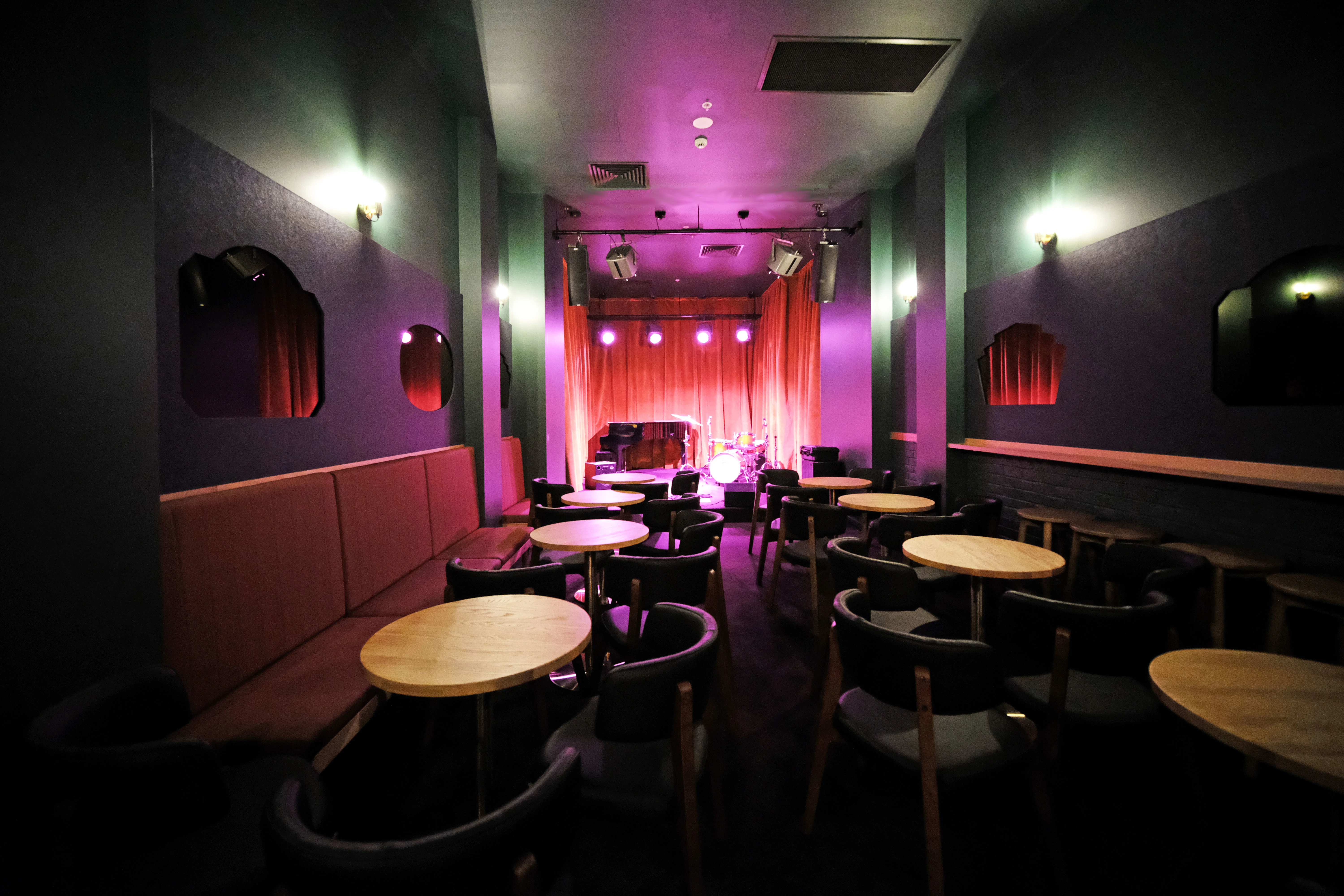 narrow bar with round tables and bench seats. Stage at the end of the room.
