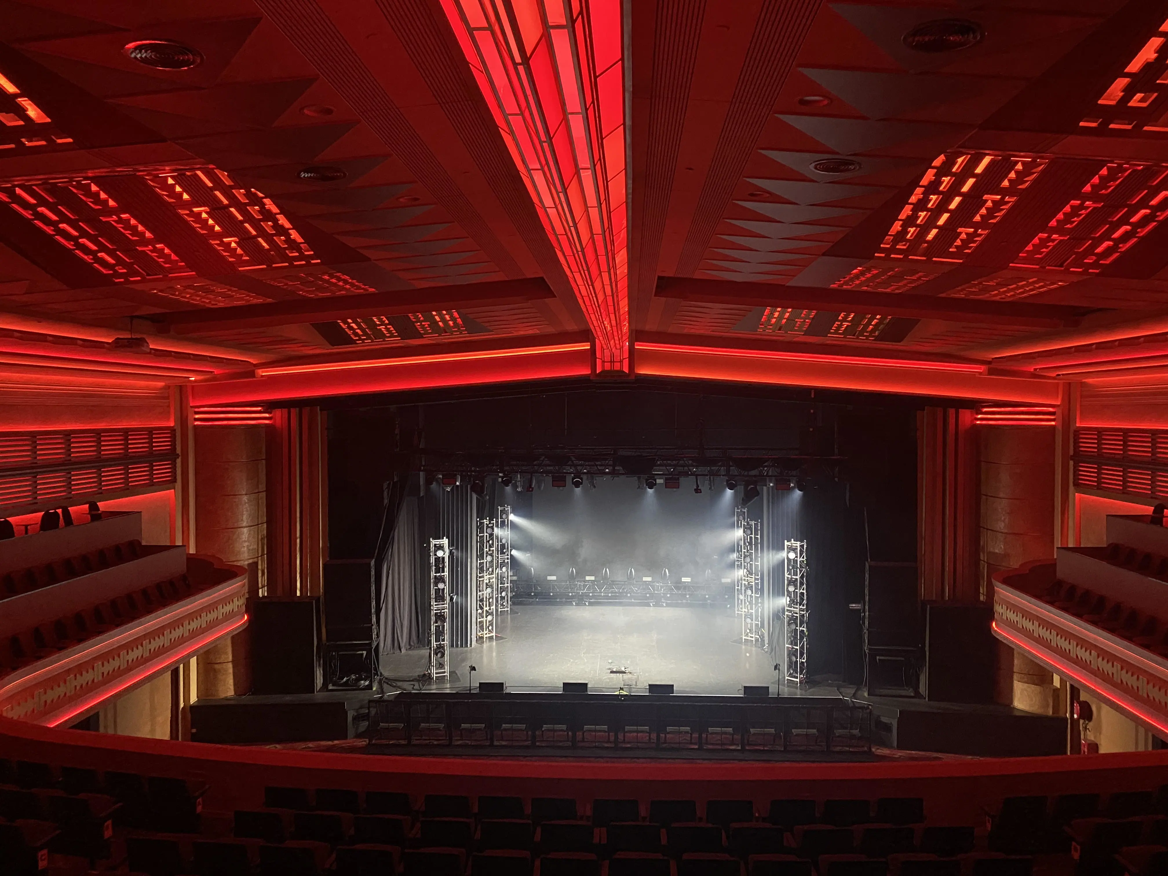 Theatre stage with white spotlights and red lights streaming on ceiling and stalls.