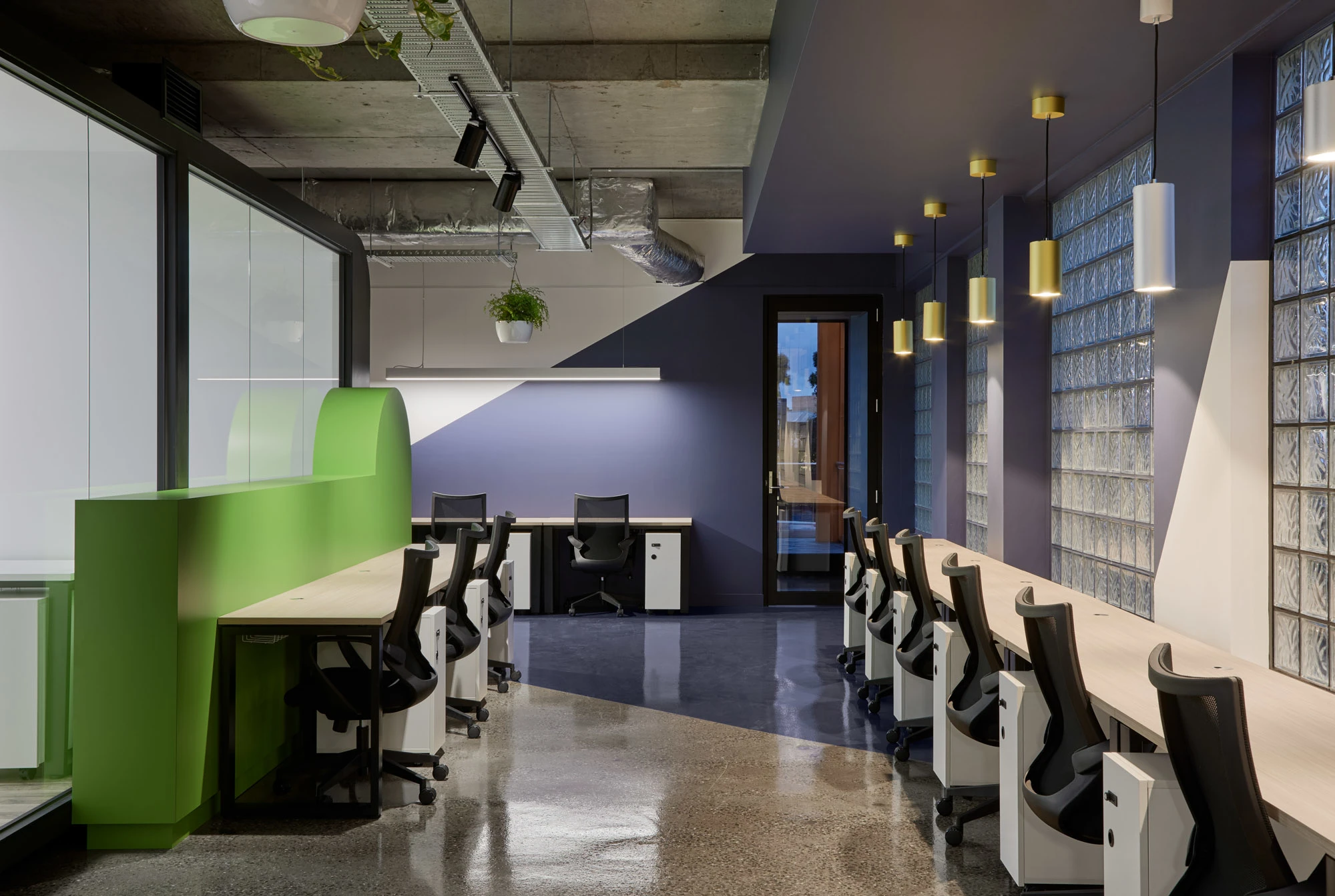 Open plan space with long desk, nine office chairs, Purple wall, glass bricks, green half-wall
