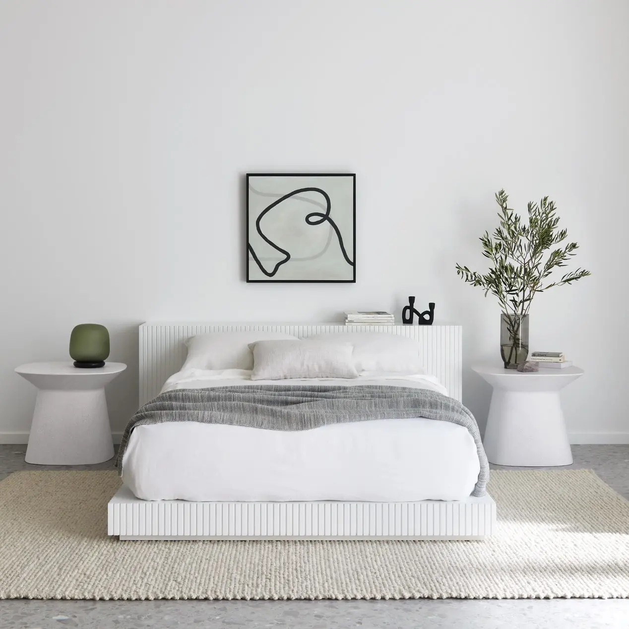 Bed and bedside tables against wall with artwork featured. Small chair beside window. 