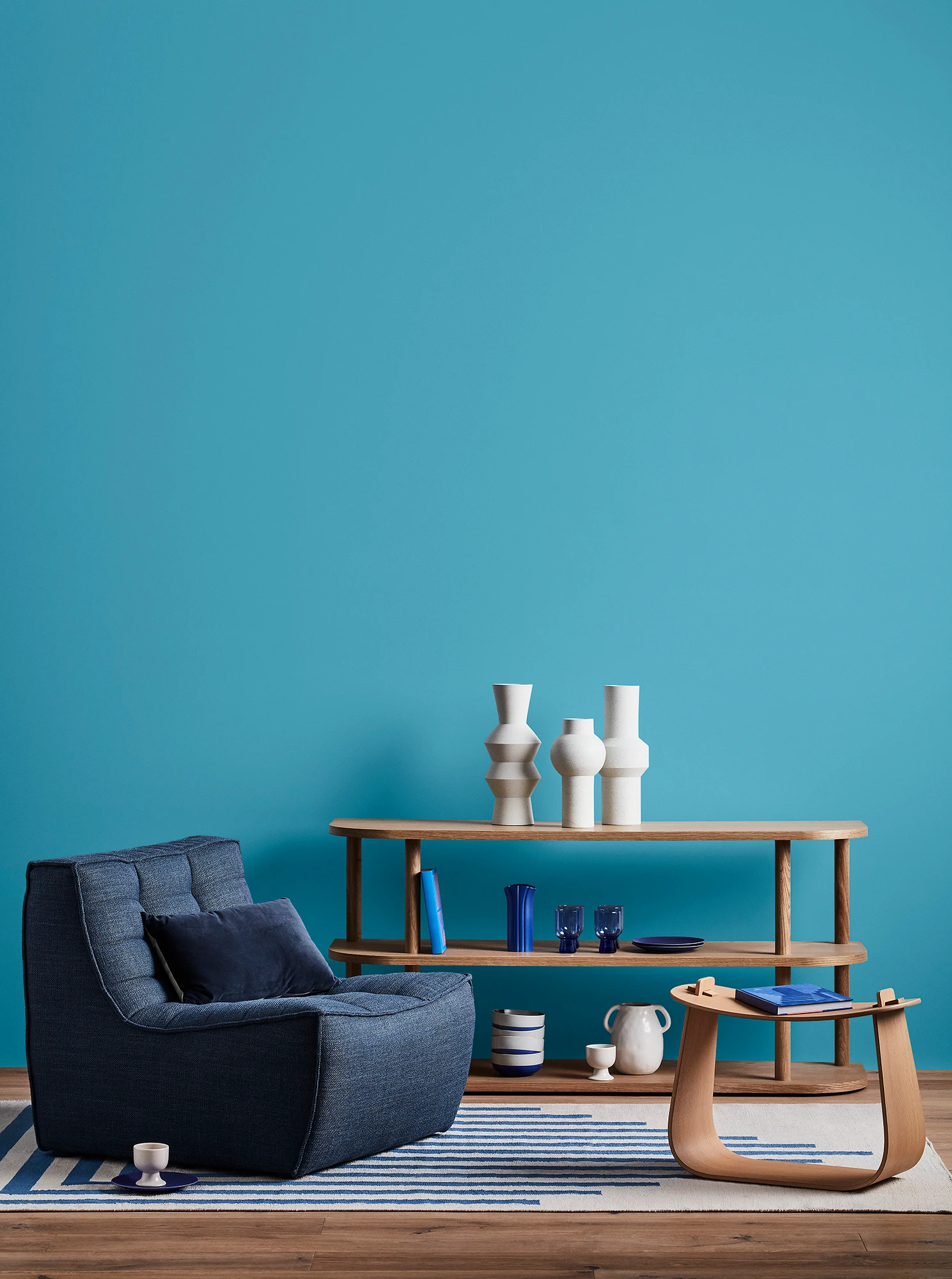 Blue living room with blue armchair, wooden coffee table and shelves with blue and white decor. 