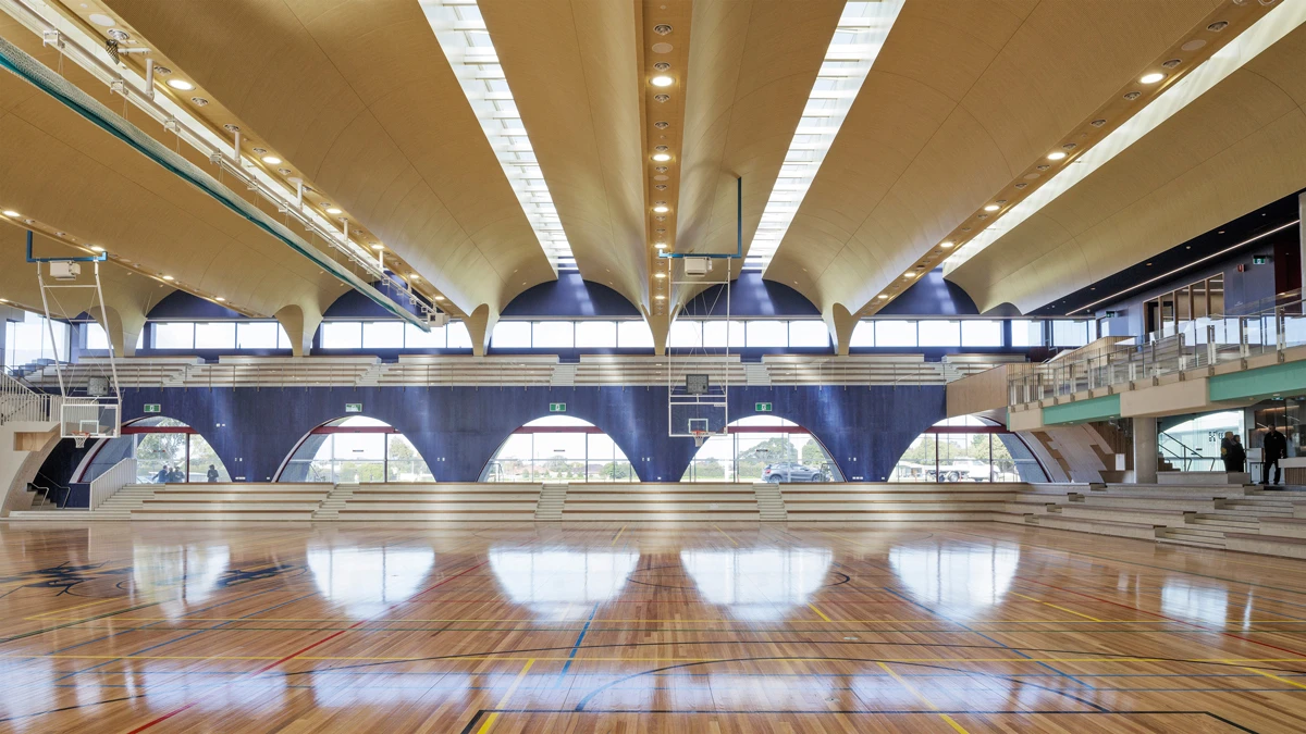 Indoor gymnasium with high roofs and tiered stairs/seating at sides. 