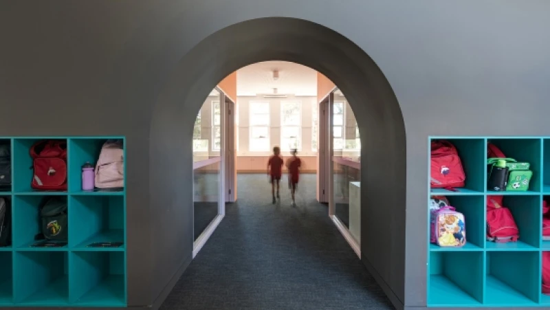 Grey wall and archway flanked by teal cube bookshelves containing childrens' ackpacks