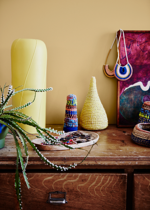 Yellow wall. Yellow vase, jewellery and small woven vessels on timber bedroom dresser