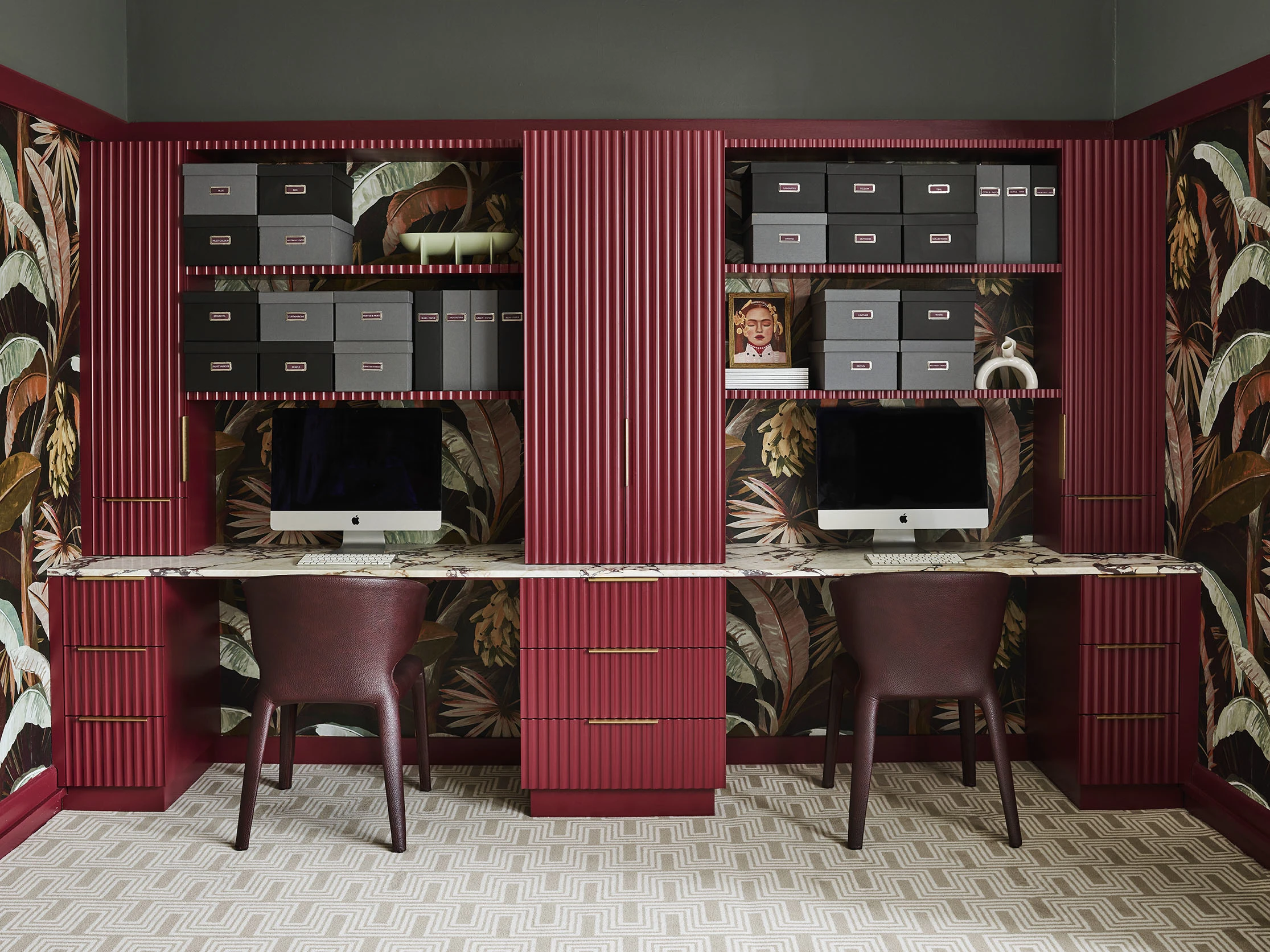 Study with wallpaper, maroon cabinets and drawers, computers, shelving with storage boxes.