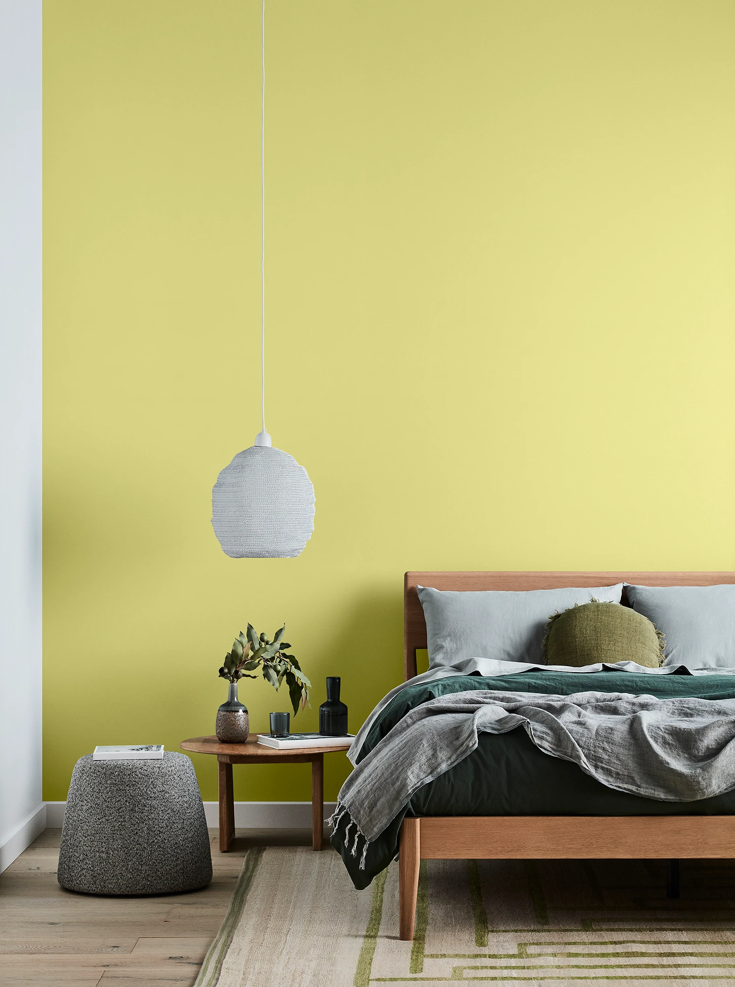 Yellow bedroom with timber bed, grey bedlinens, white pendant light and timber side table.