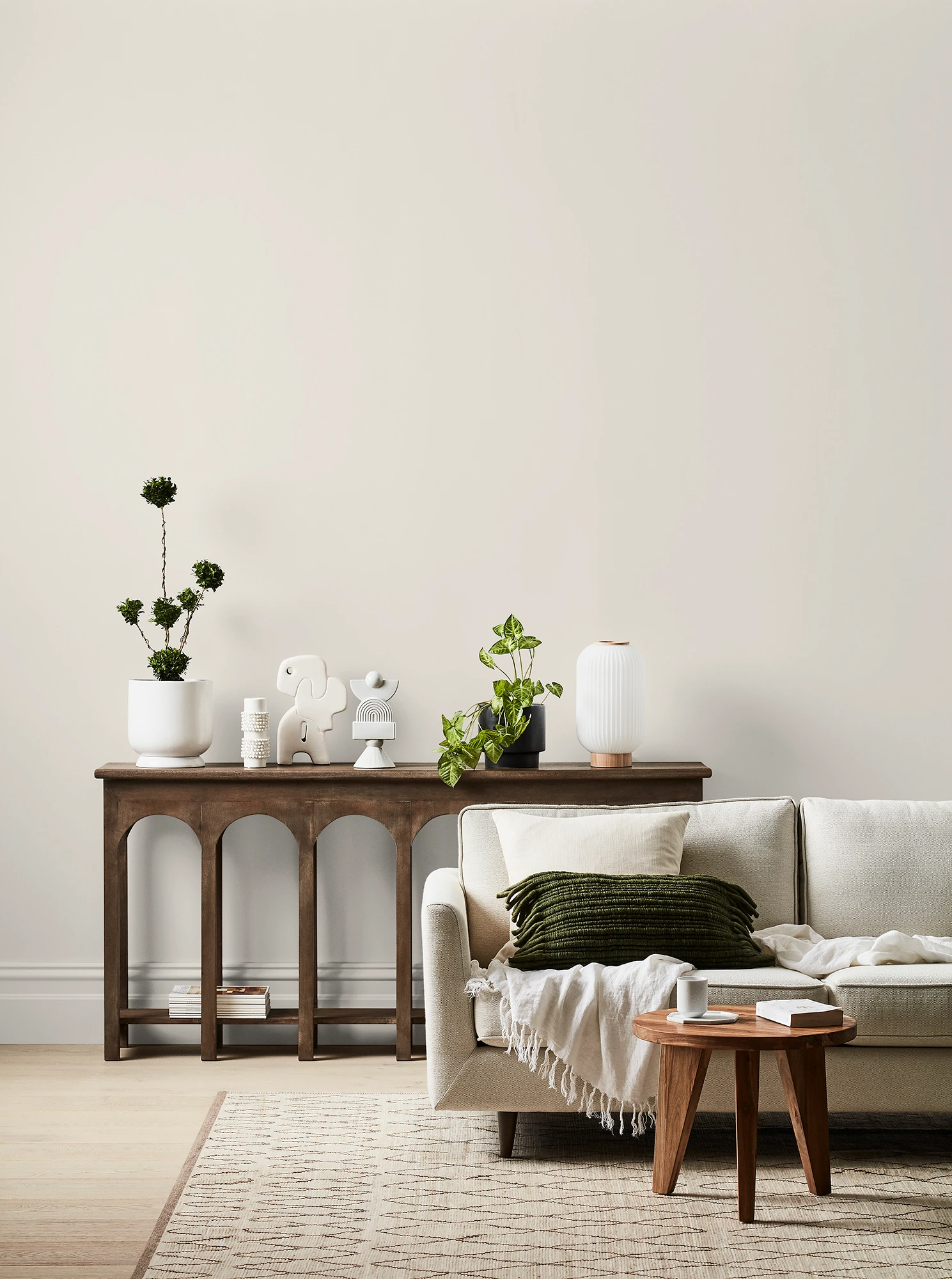 White living room with cream couch, timber side table and timber table with ornaments and plants.