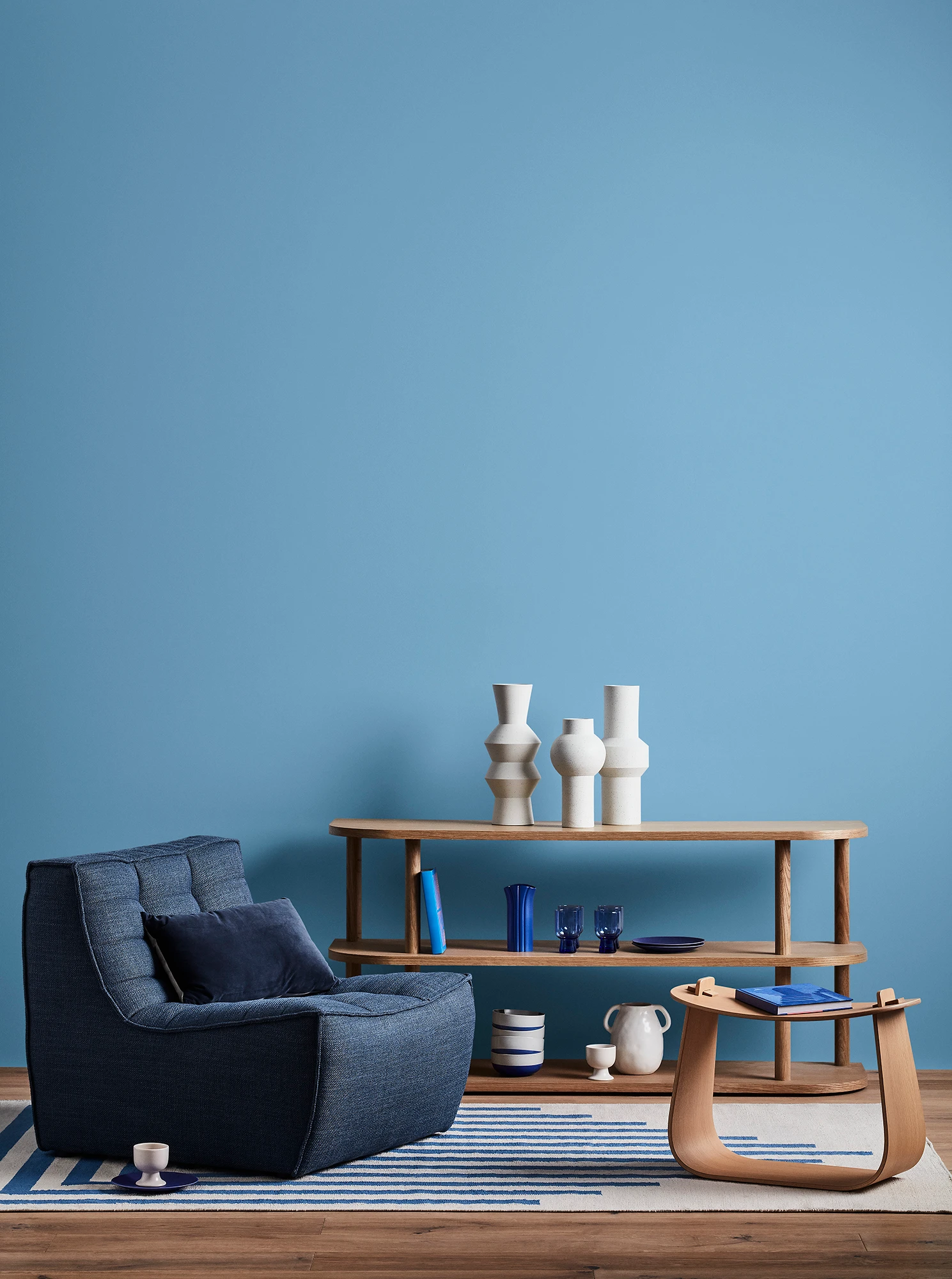 Blue living room with blue armchair, wooden coffee table and shelves with blue and white decor. 