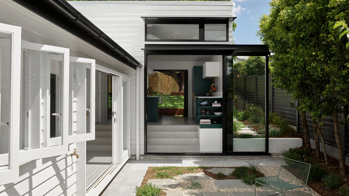 Exterior of home with open windows and open door area leading into tiered open-plan kitchen/living.