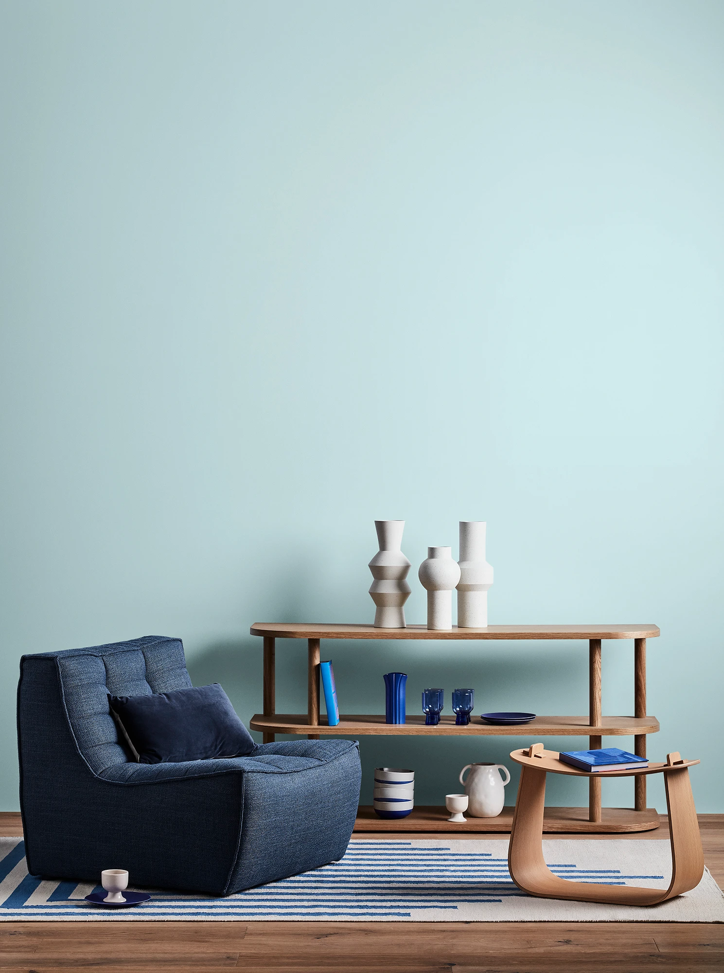 Blue living room with blue armchair, wooden coffee table and shelves with blue and white decor. 