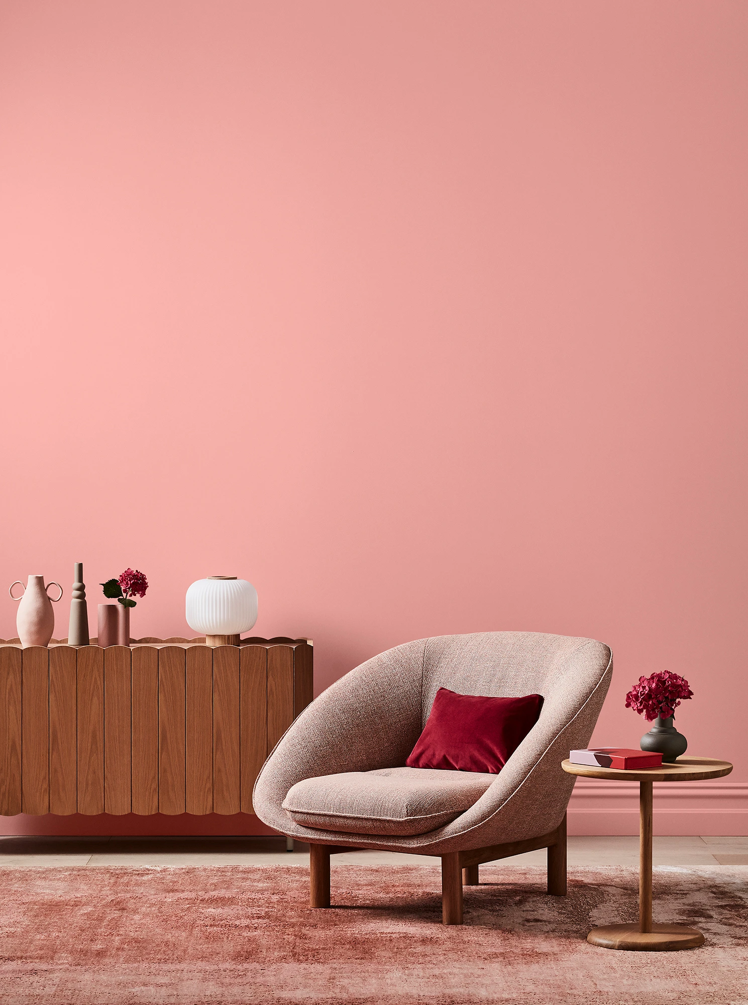 Deep pink living room with pink armchair, wooden side table and sideboard with white and pink decor.