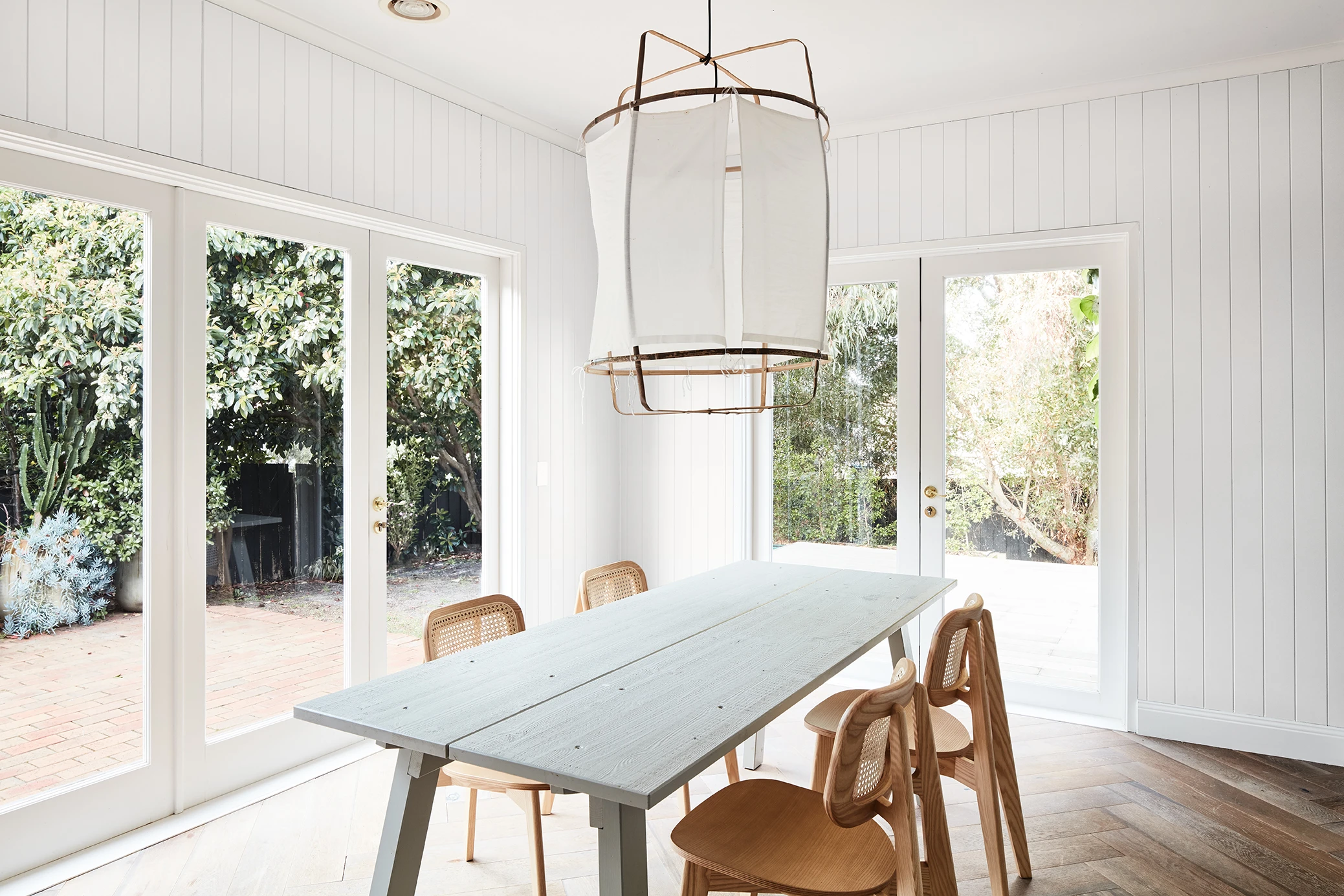 White dining room with VJ panelling on the walls, wooden dining table and bifold doors.