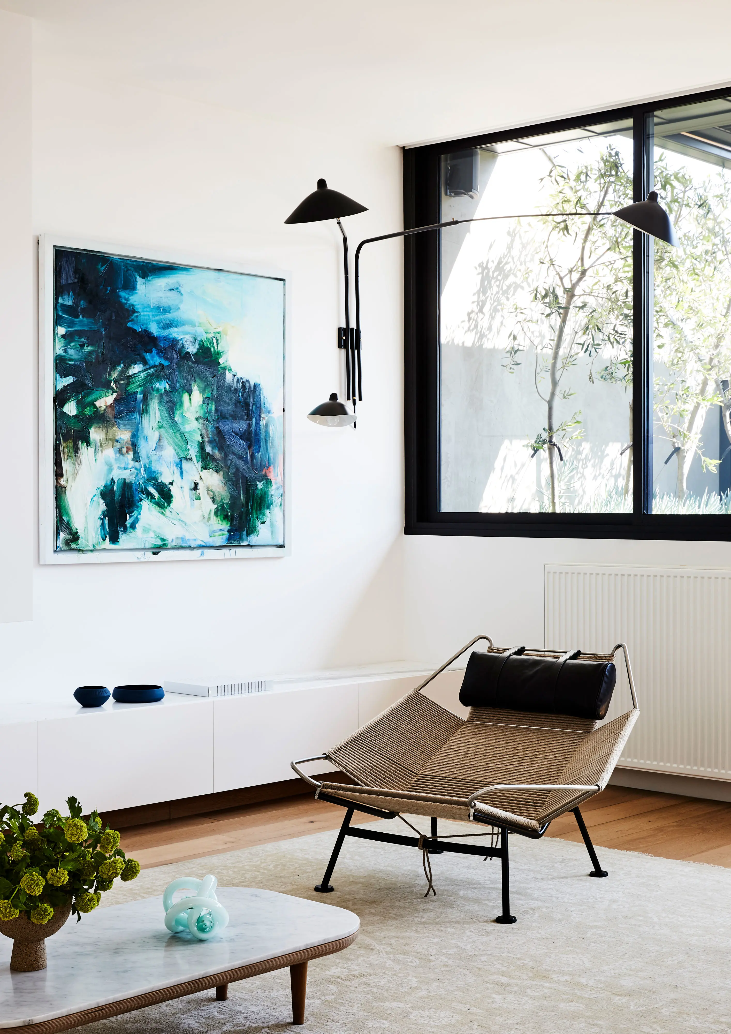 White modern living room with blue artwork and angular chair.