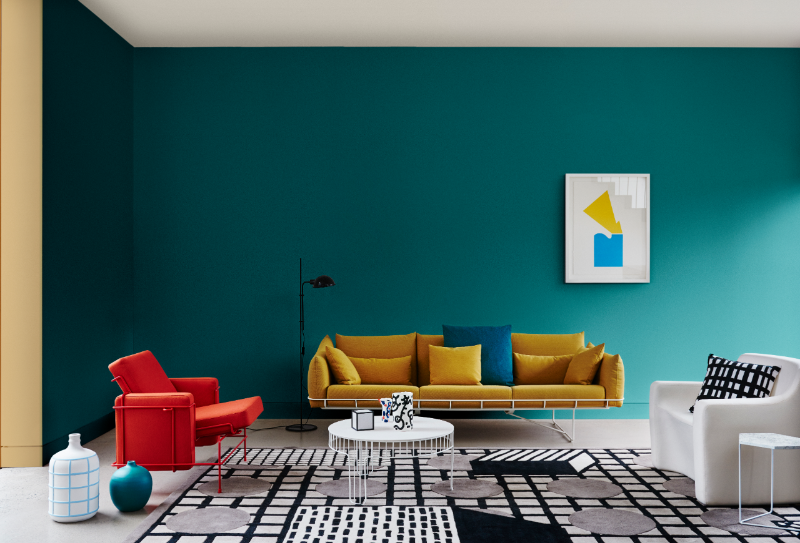 Teal living room with red chair, brown couch, black and white rug, black floor lamp, cushions, white round coffee table, artwork by Marnie Gilder, white armchair 