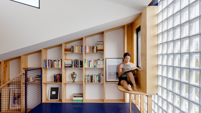 Upstairs reading nook with glass brick wall and in-built sloped bookshelf