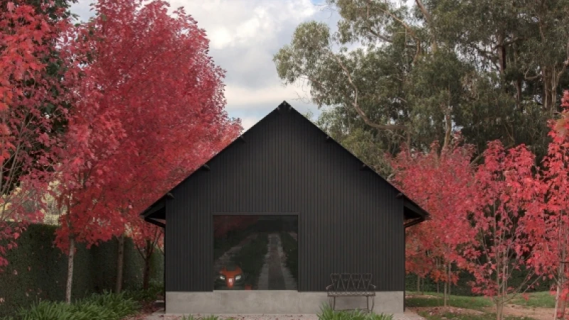 Black barn-style house surrounded by red deciduous trees